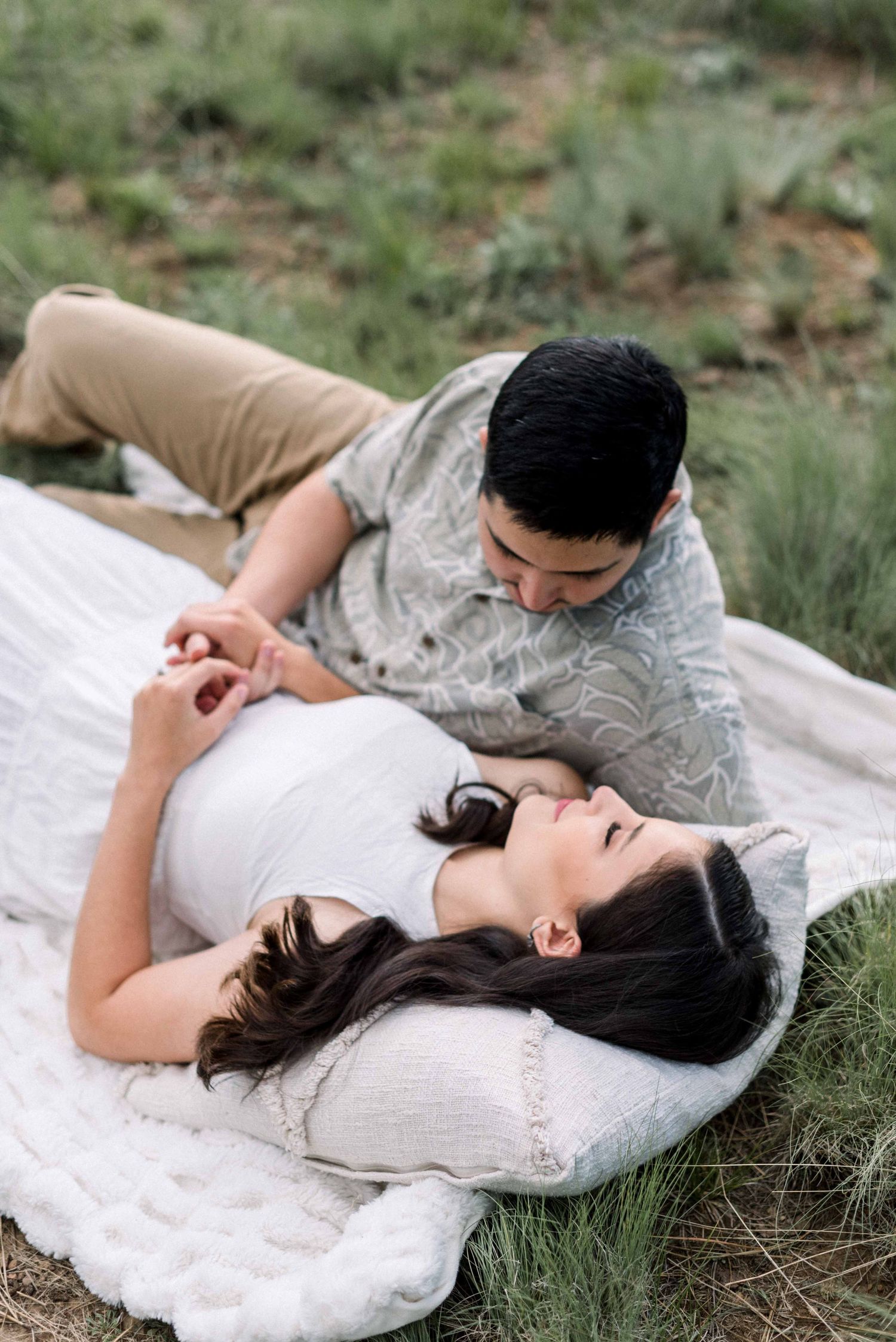 Romantic moment captured on white blanket in grassy outdoor setting.