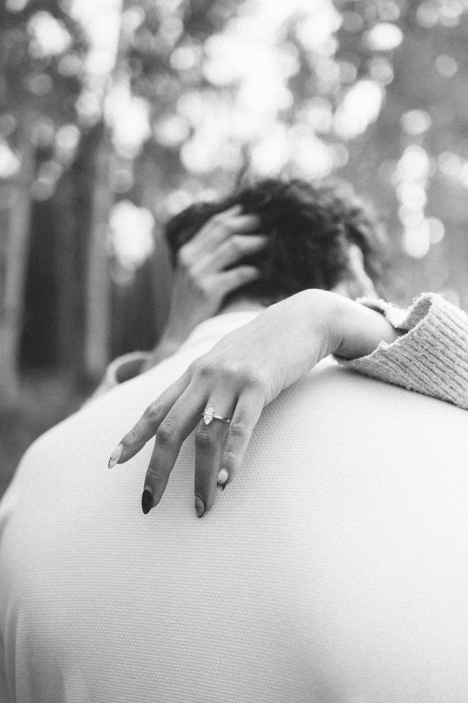 Close-up of hands with engagement ring resting on sweater in black and white.