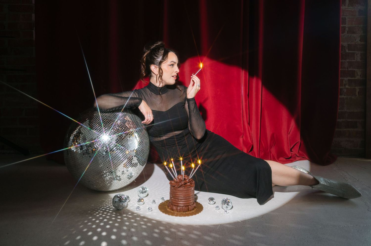 Birthday celebration scene with chocolate cake and disco ball in dark room with red curtain.