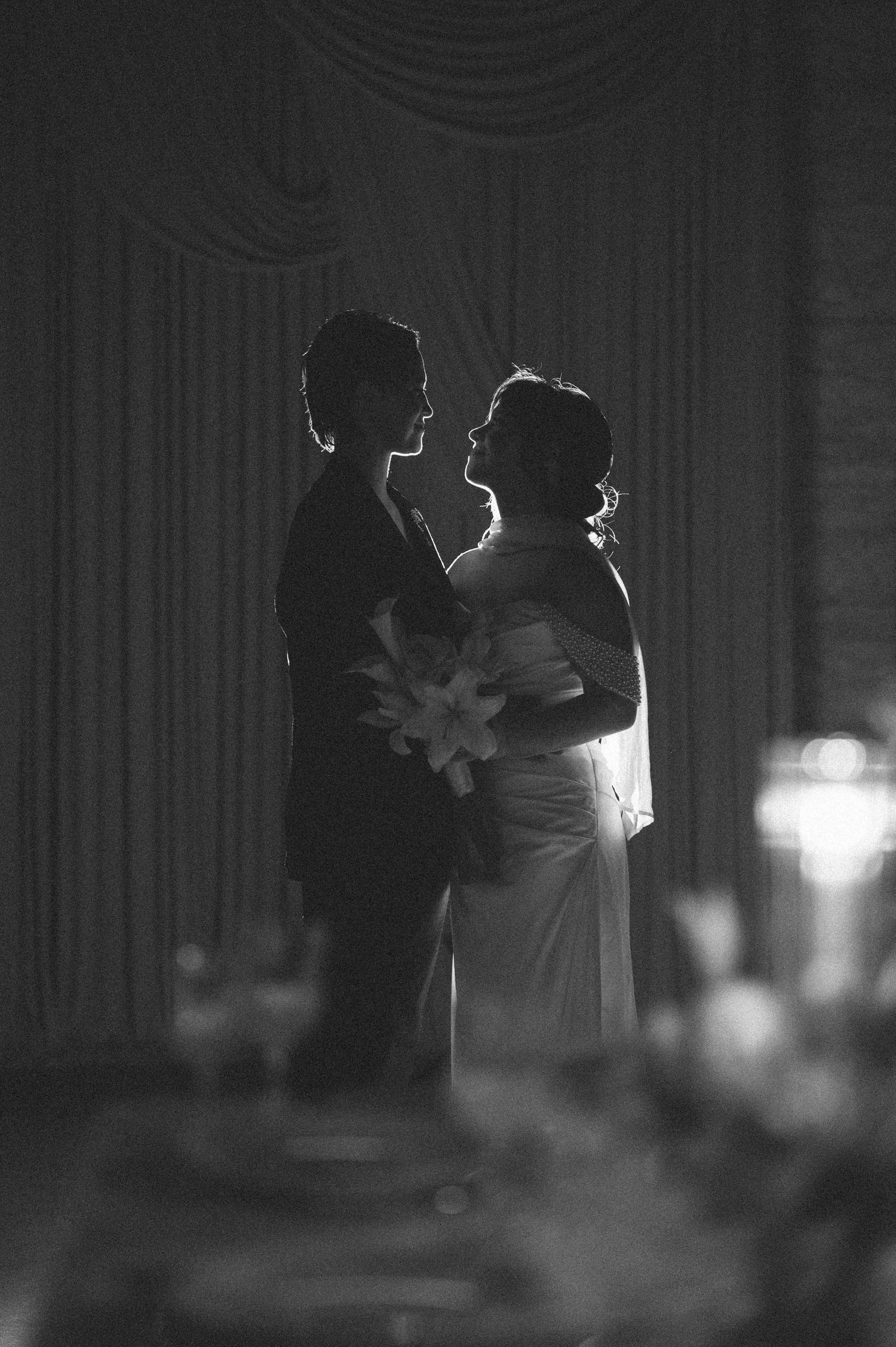 A romantic black and white silhouette of a couple sharing an intimate moment during their first dance at a wedding reception.