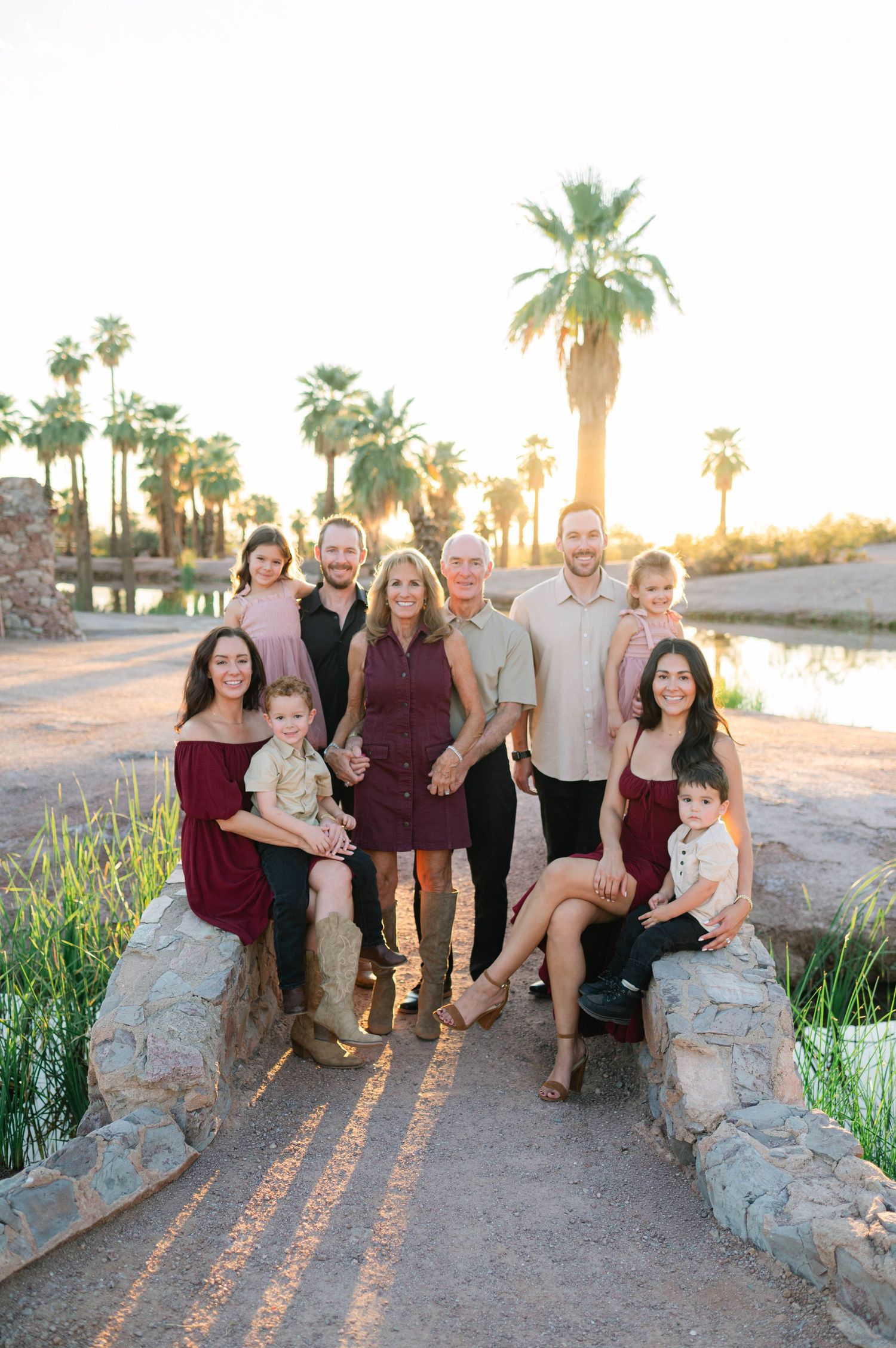 A group poses together on a stone bridge at sunset with palm trees and a lake in the background.