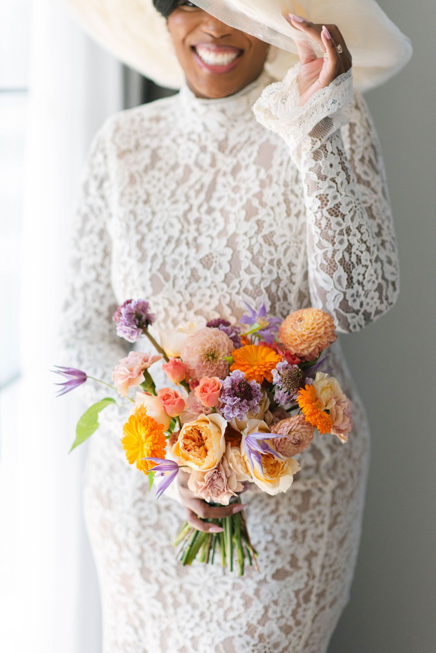 A colorful bouquet of orange, pink and purple flowers held against a white lace dress.