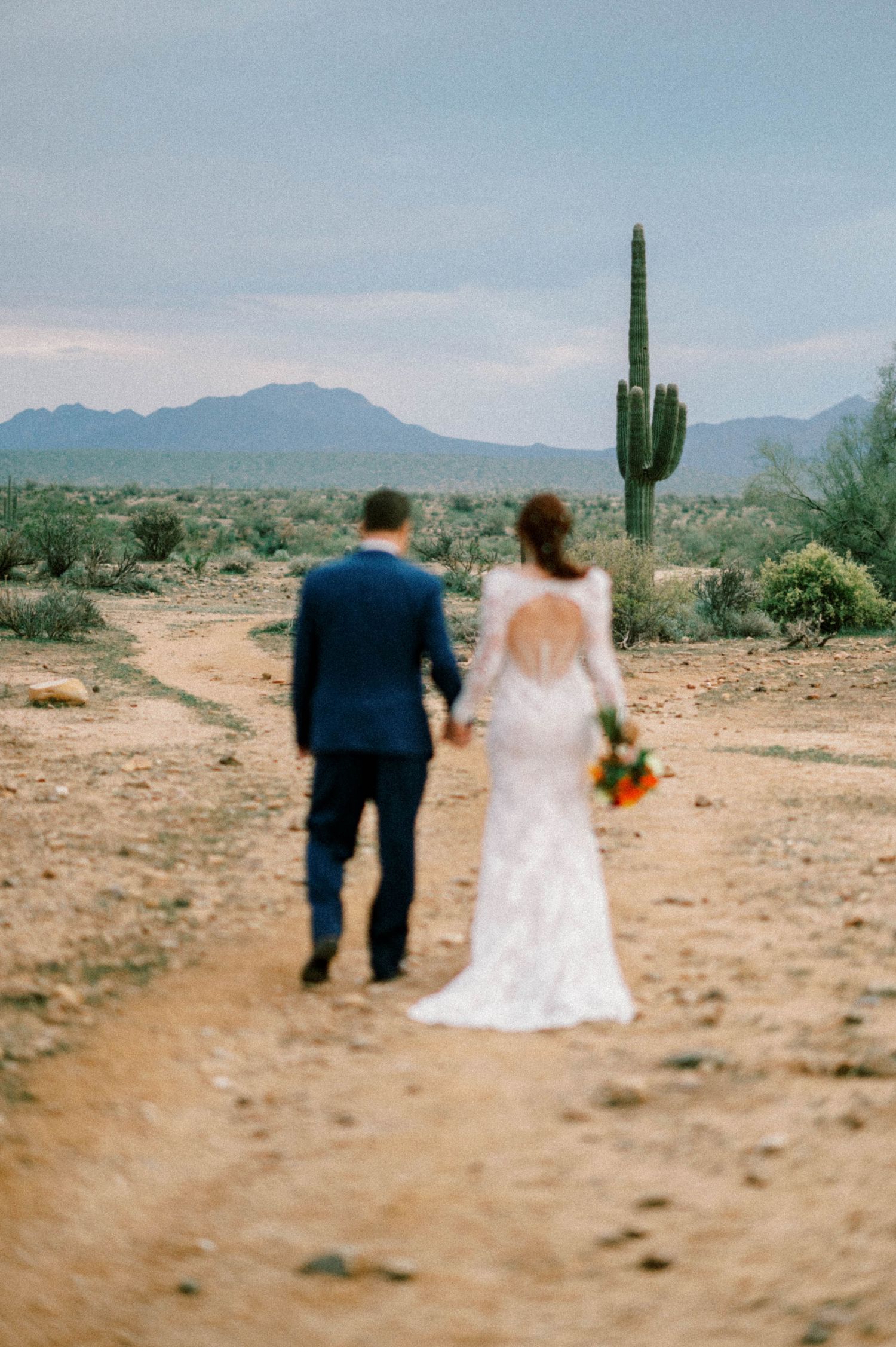 Desert wedding photos with couple walking among saguaro cacti in Arizona landscape.