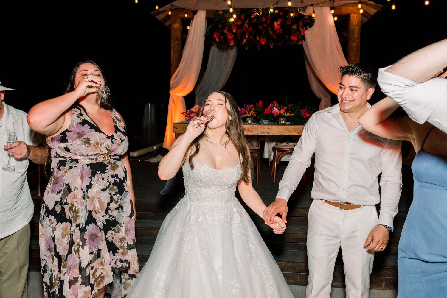 Wedding guests laughing and dancing with the bride at a nighttime outdoor celebration.
