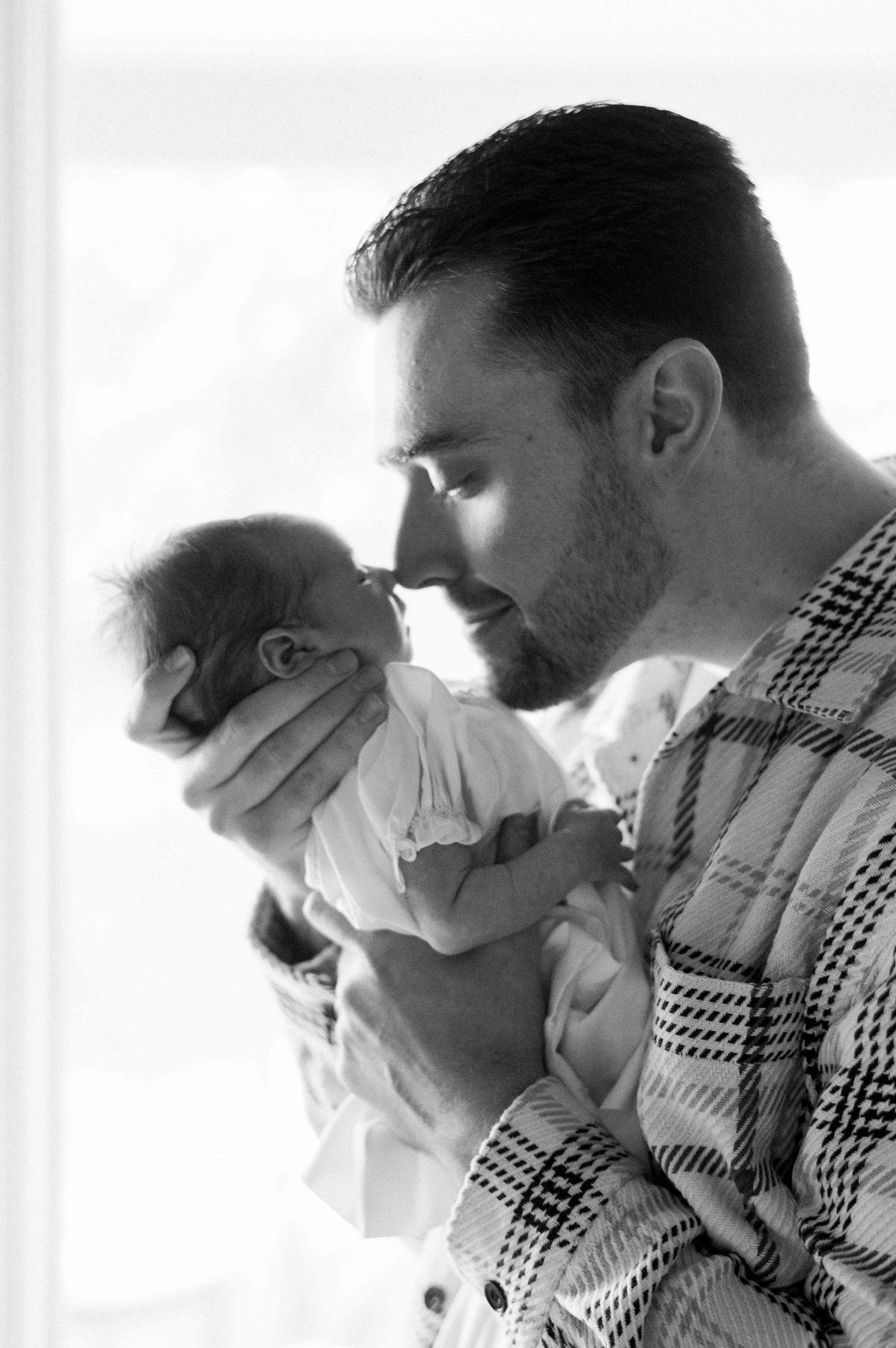 A tender black and white portrait of a newborn baby being held in plaid-shirted arms.