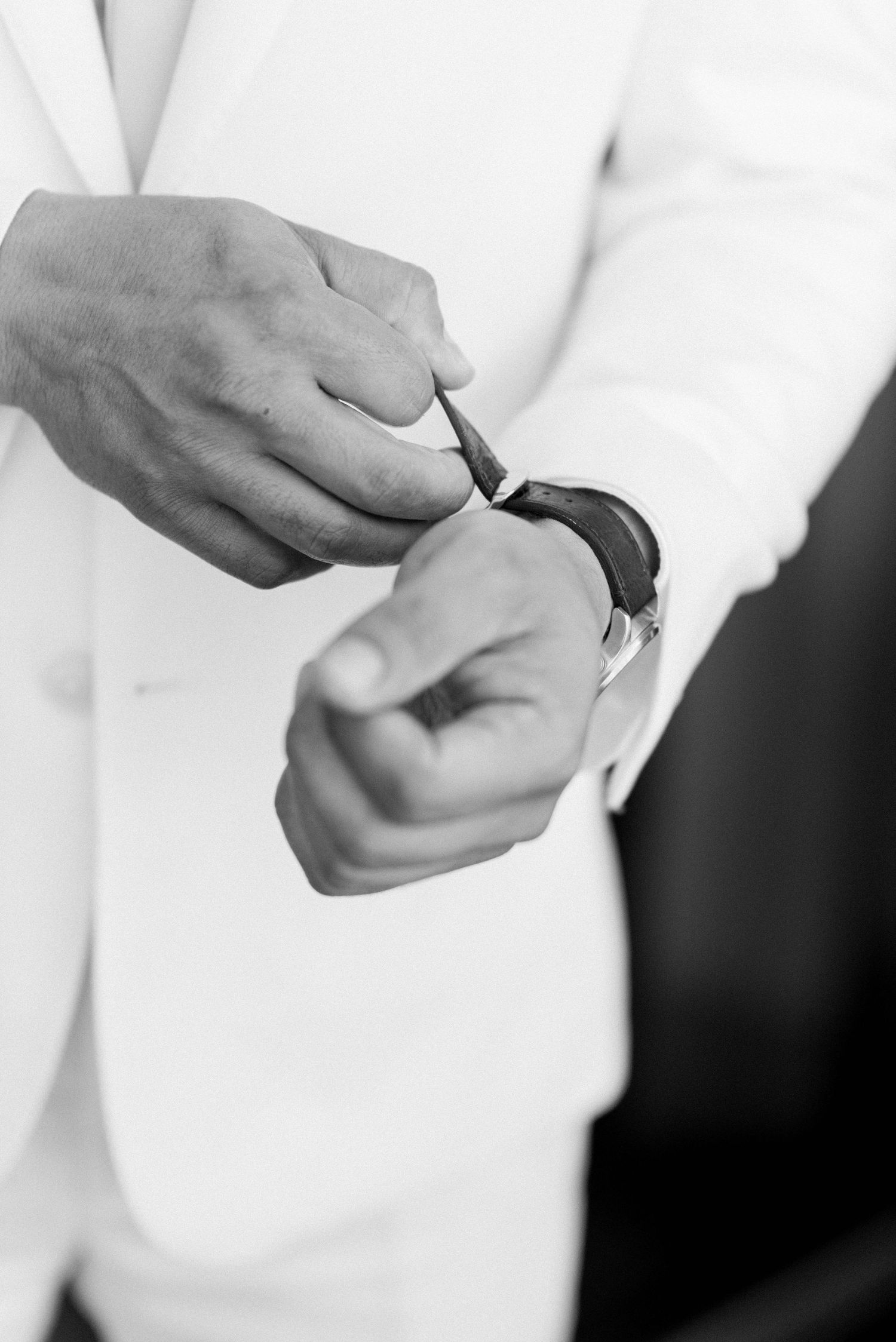 Close-up of hands adjusting a watch while wearing a crisp white suit jacket.