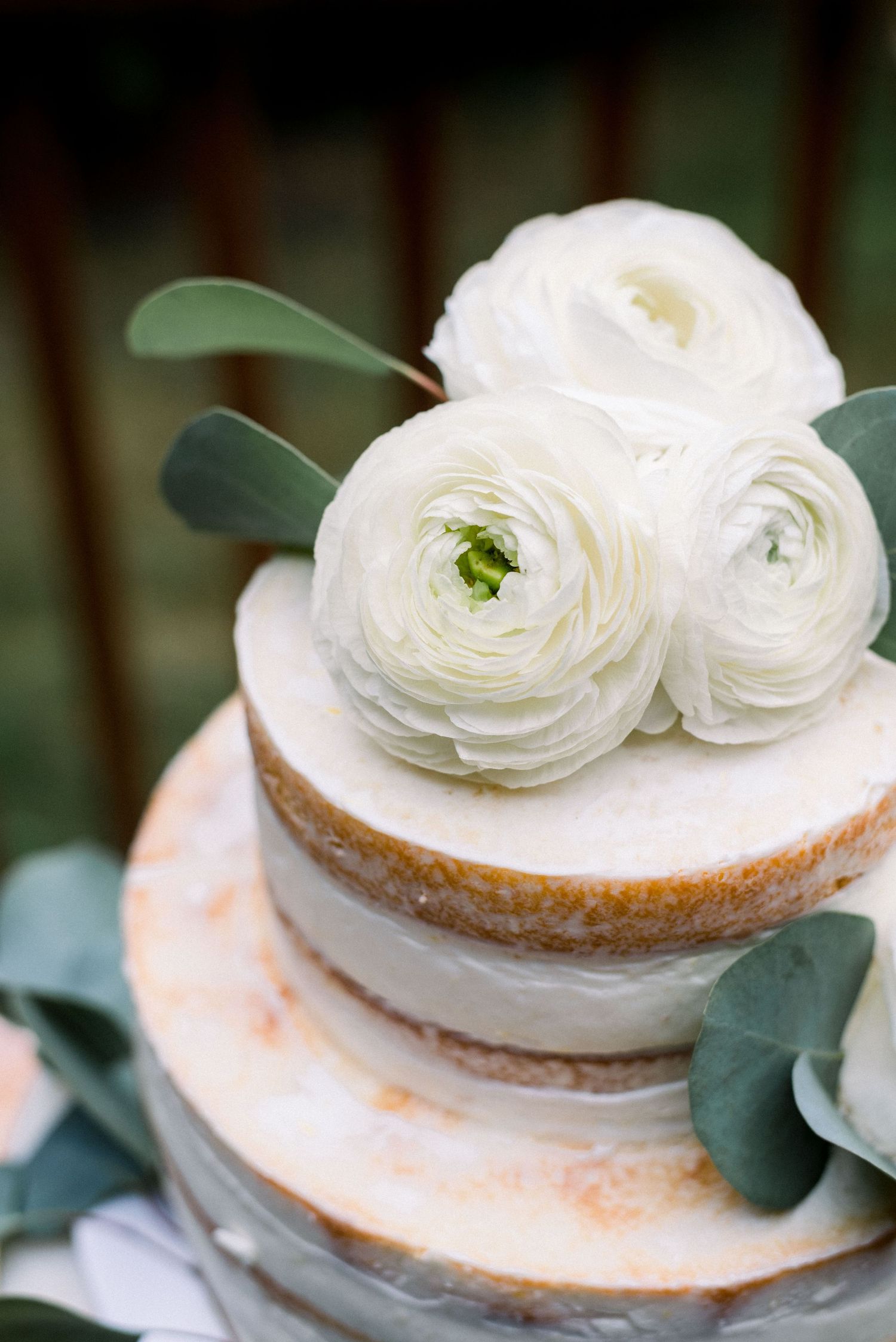 Elegant two-tier white wedding cake topped with fresh ranunculus flowers and eucalyptus.