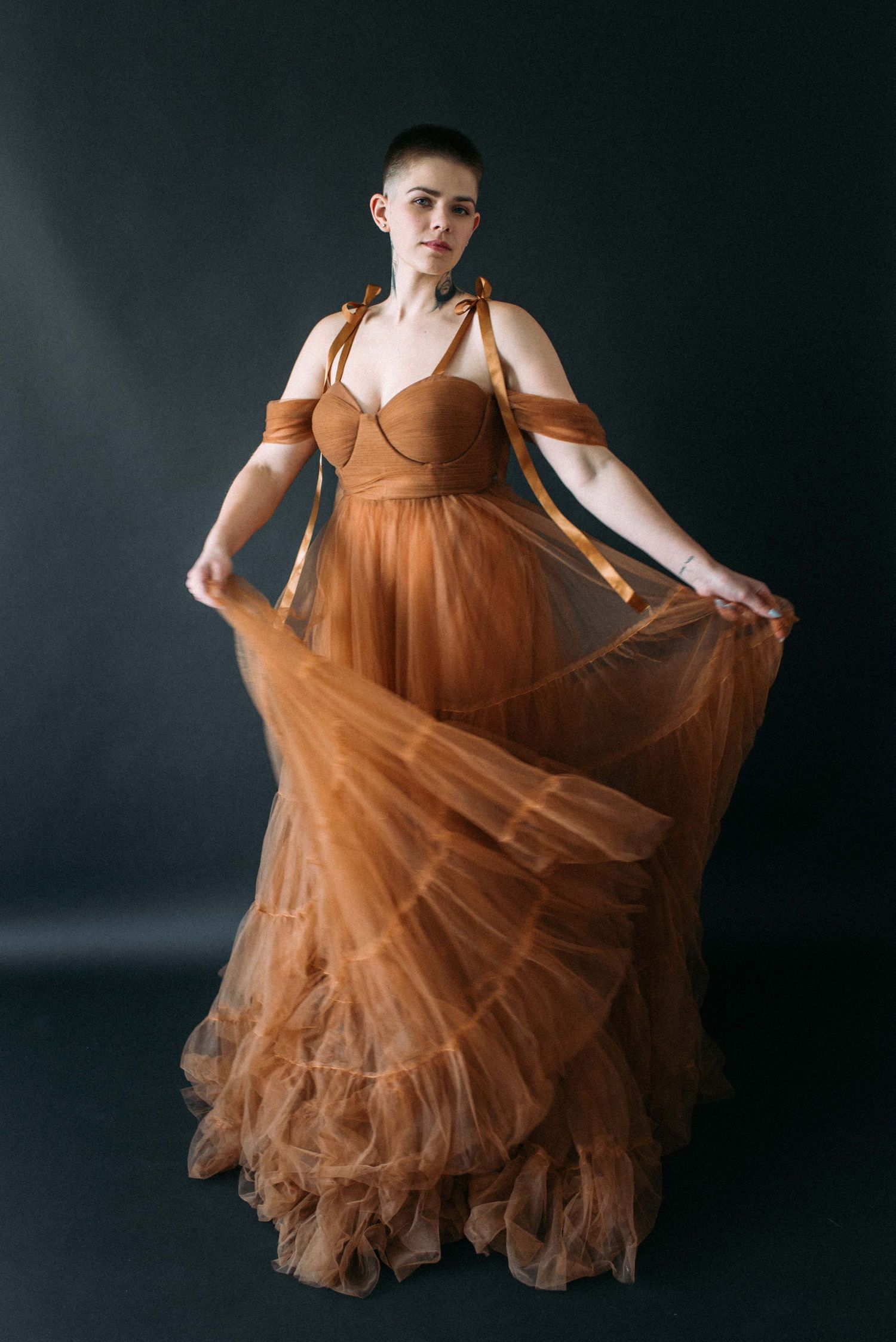 Someone holds out the layers of a brown tulle dress in an elegant studio portrait.