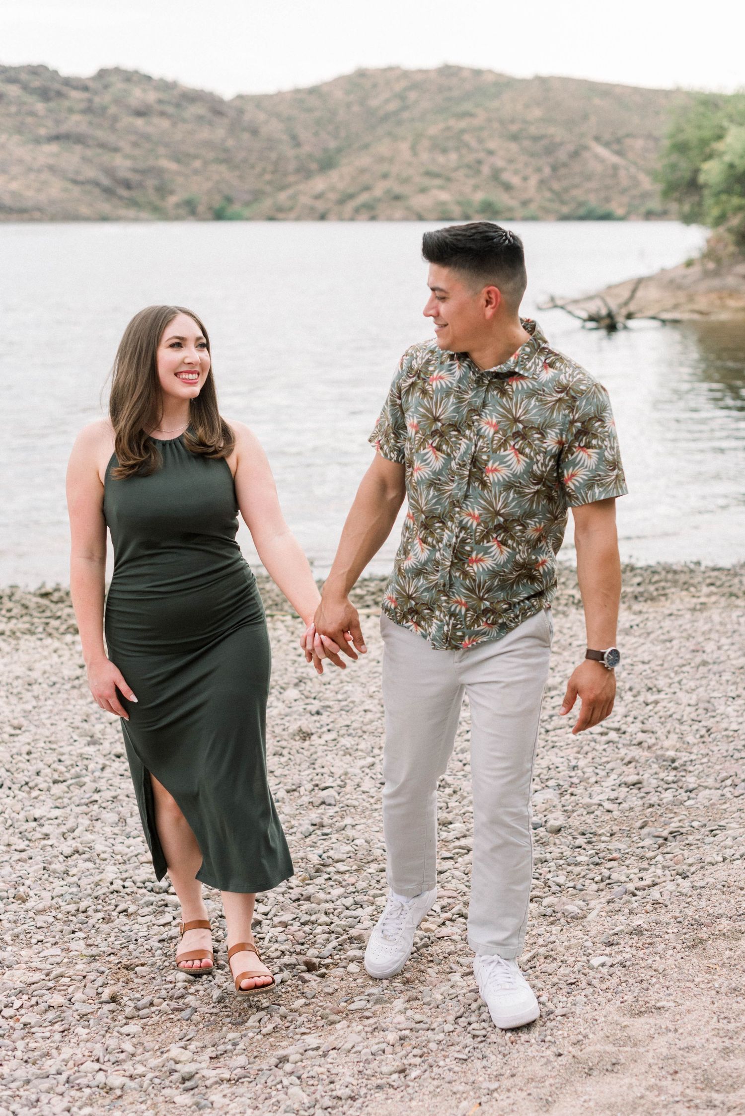 A couple walks together along a rocky shoreline wearing coordinated outfits near a lake at sunset.