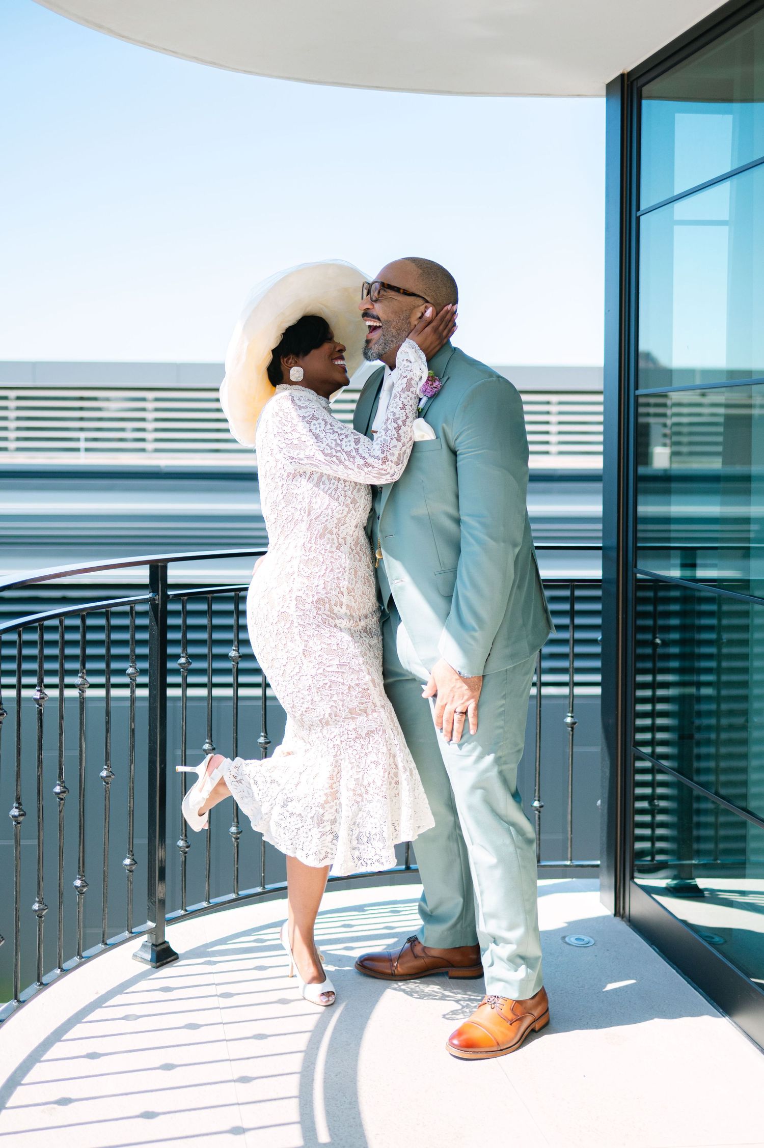 Couple in wedding attire embrace on a balcony overlooking the ocean.