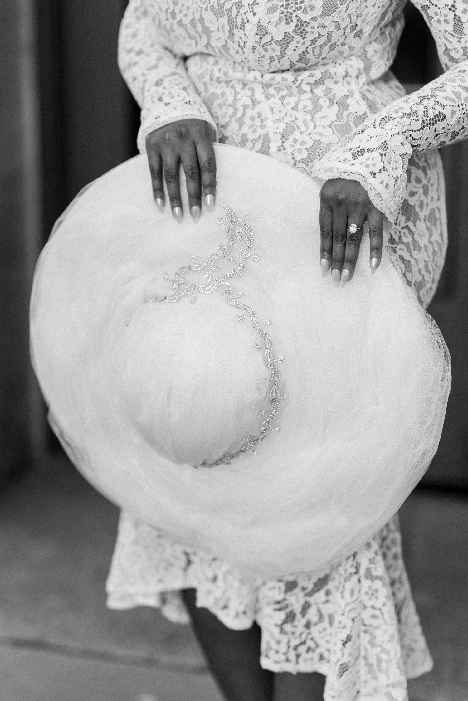 A close-up view of a white lace wedding dress with delicate floral details and tulle fabric swirling in motion.