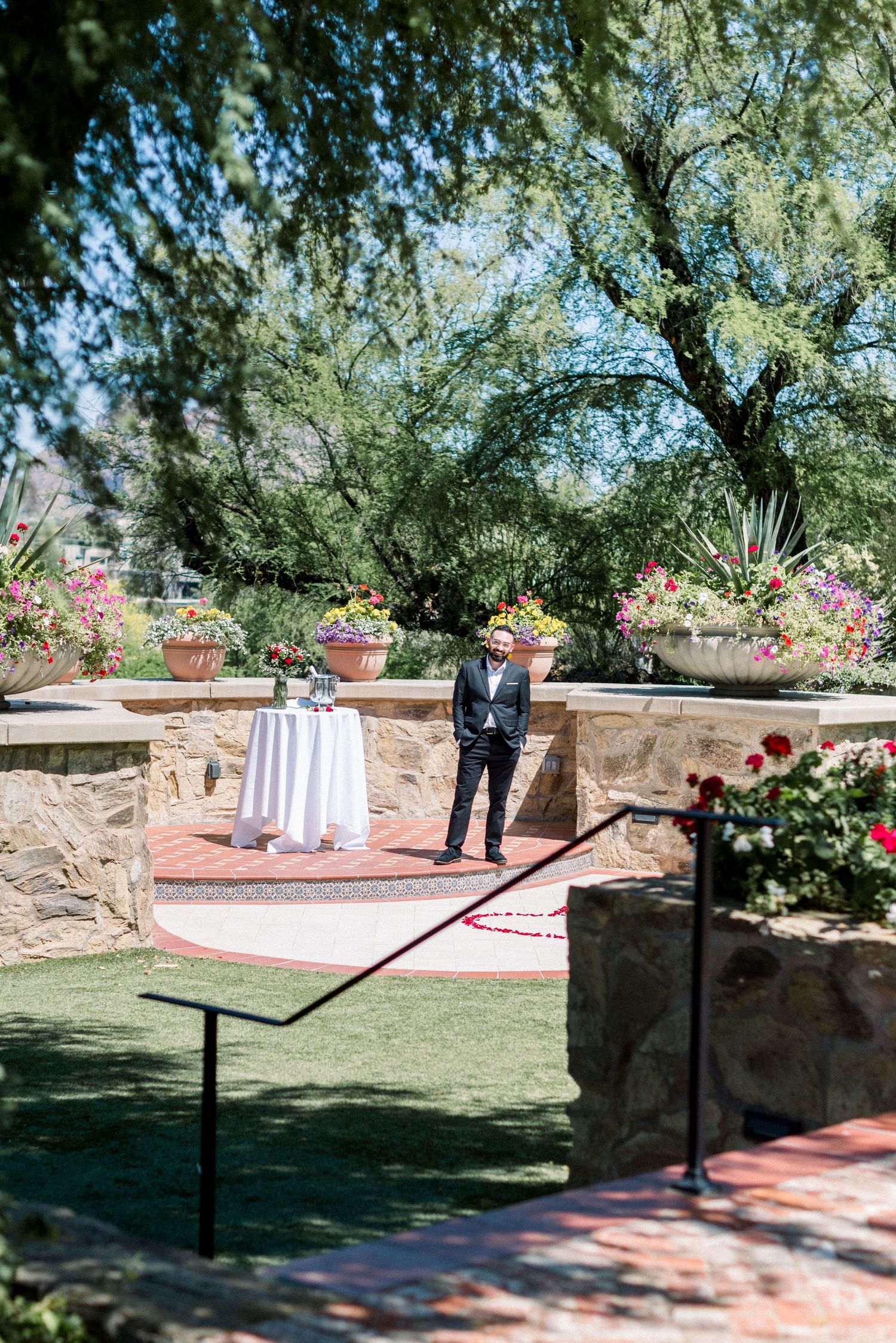 Groom waiting at outdoor wedding venue with table and floral decorations.