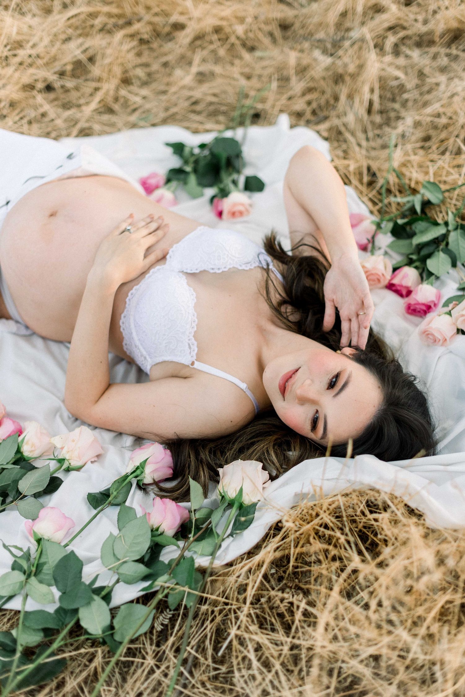 Dreamy maternity photo with scattered pink roses and white lingerie.