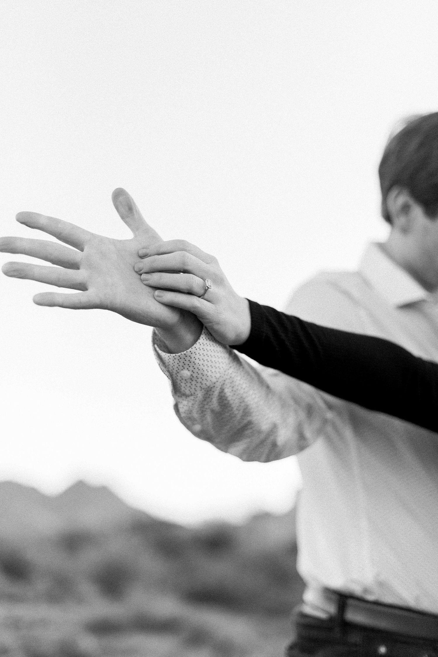Close-up black and white photo of hands showing an engagement ring.