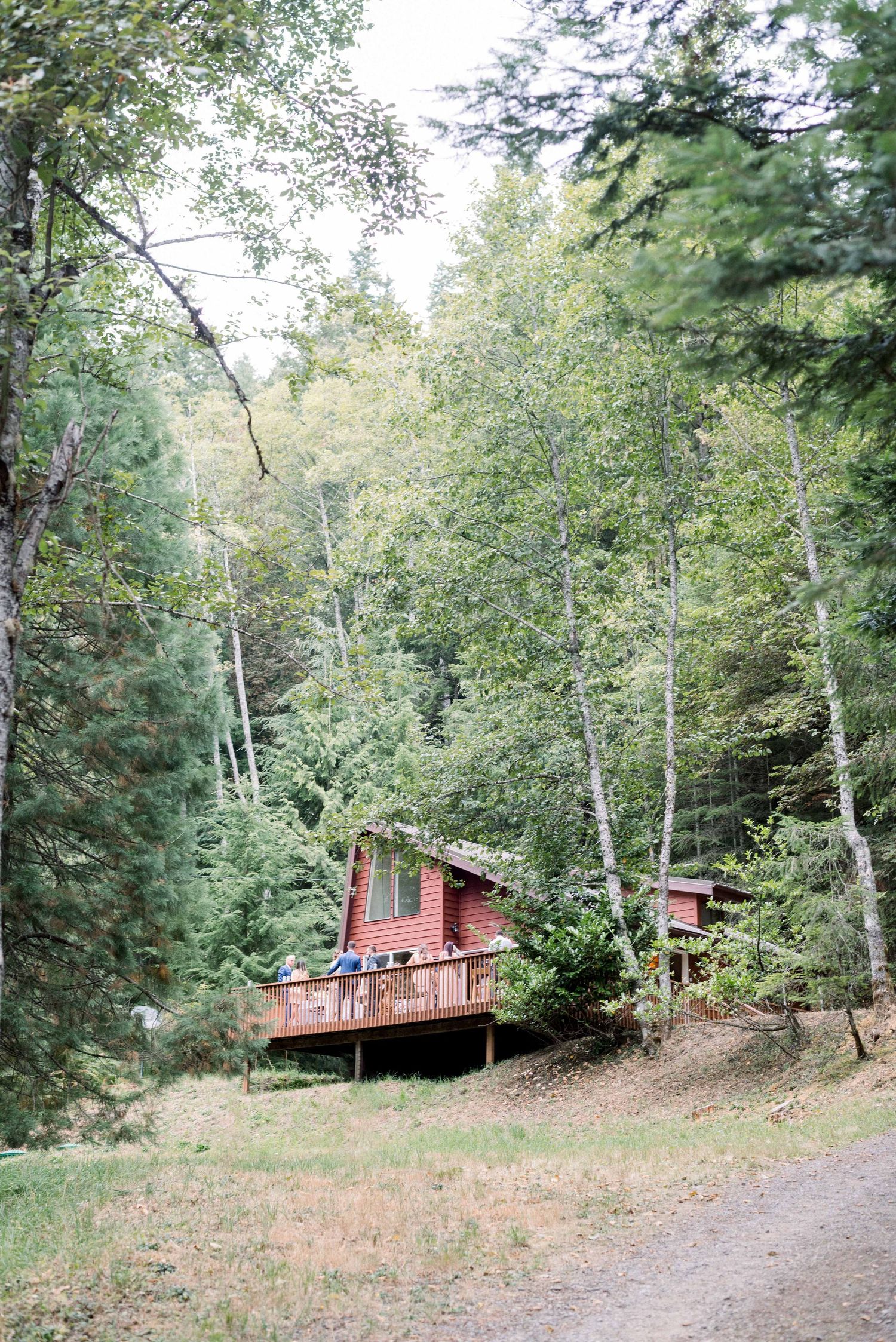 Red cabin with wooden deck nestled among tall trees in forest setting.