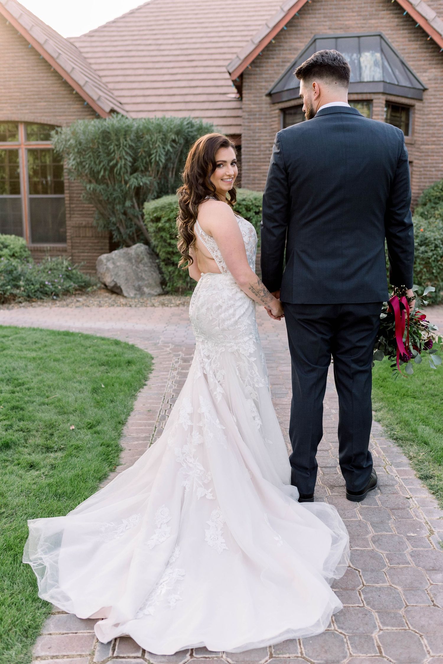 Newlyweds walking on stone path with bride's flowing white dress trailing behind.