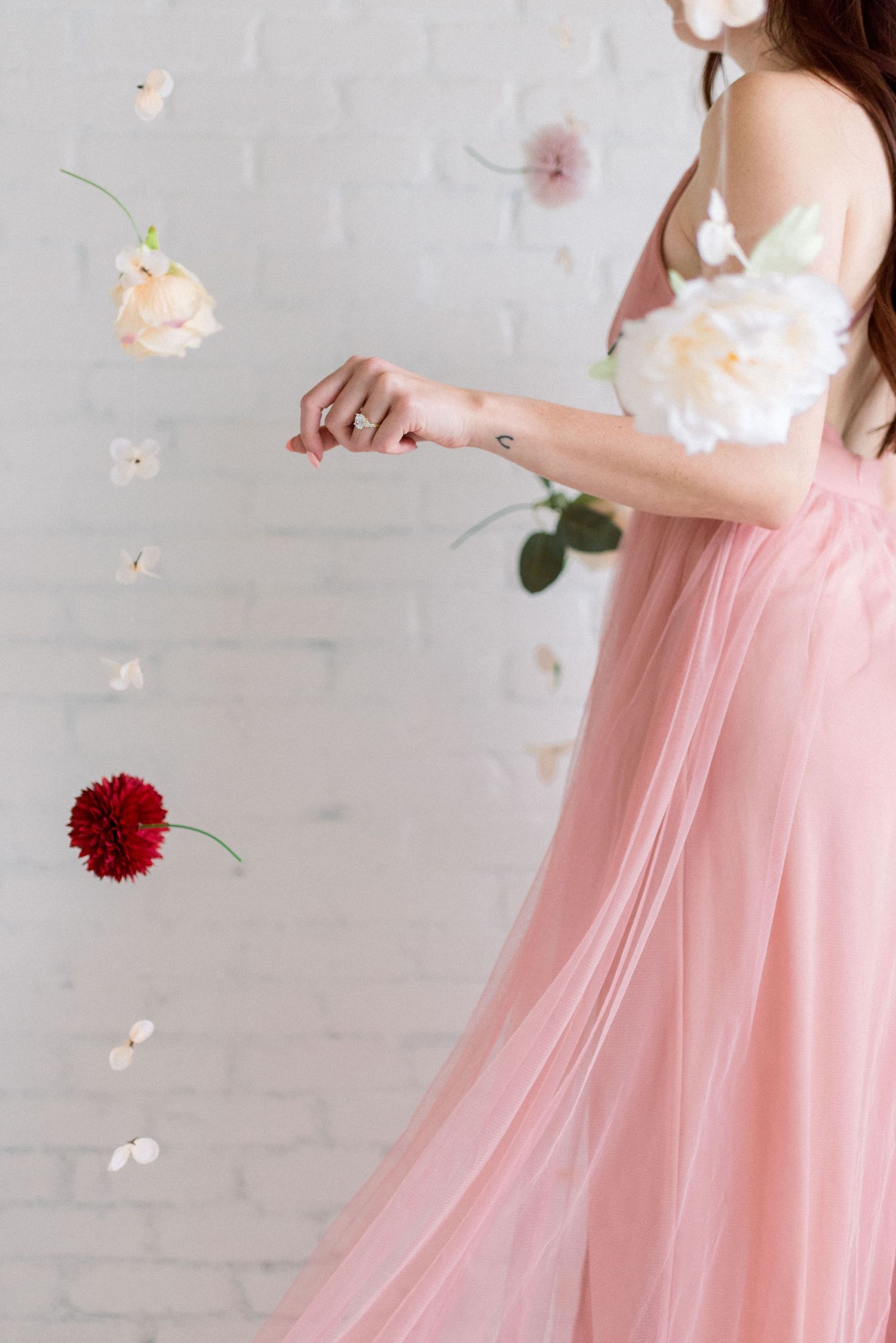 A flowing pink dress with floating flowers and petals in a romantic studio setting.