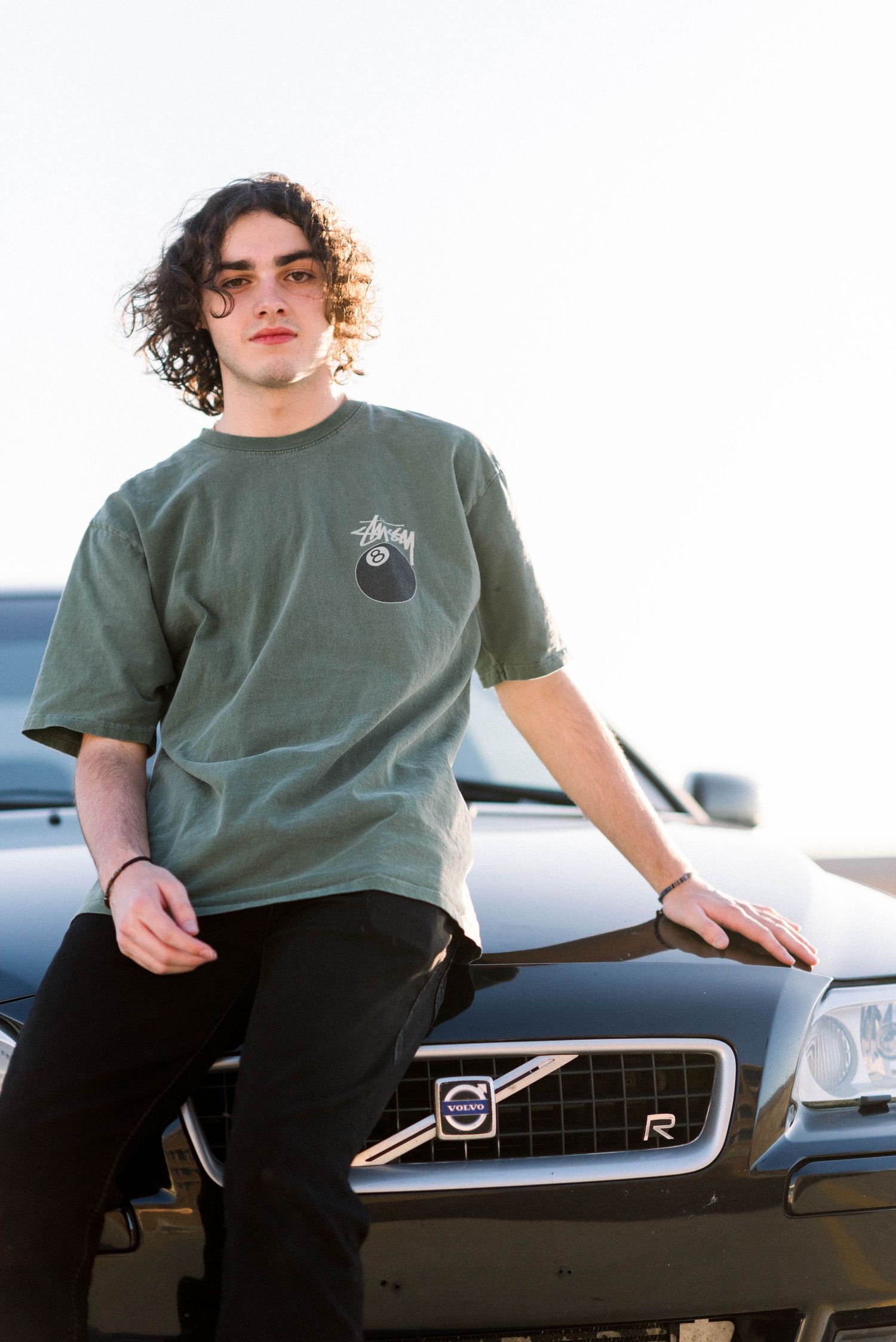 Person in green t-shirt posing on Volvo car hood with logo visible.