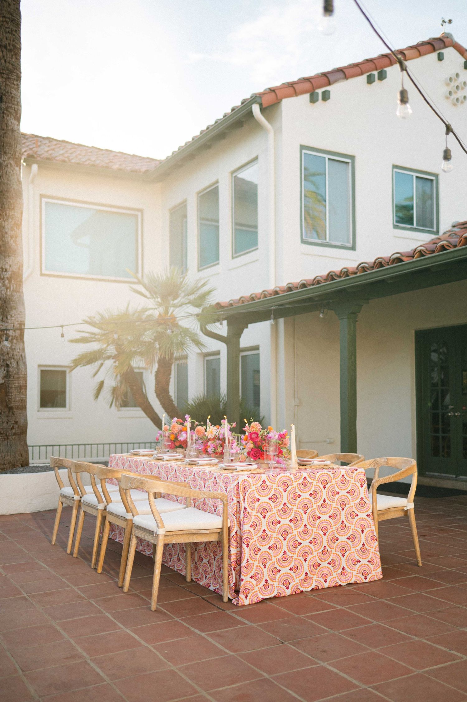 Outdoor patio with coral tablecloths and string lights set for a wedding reception.