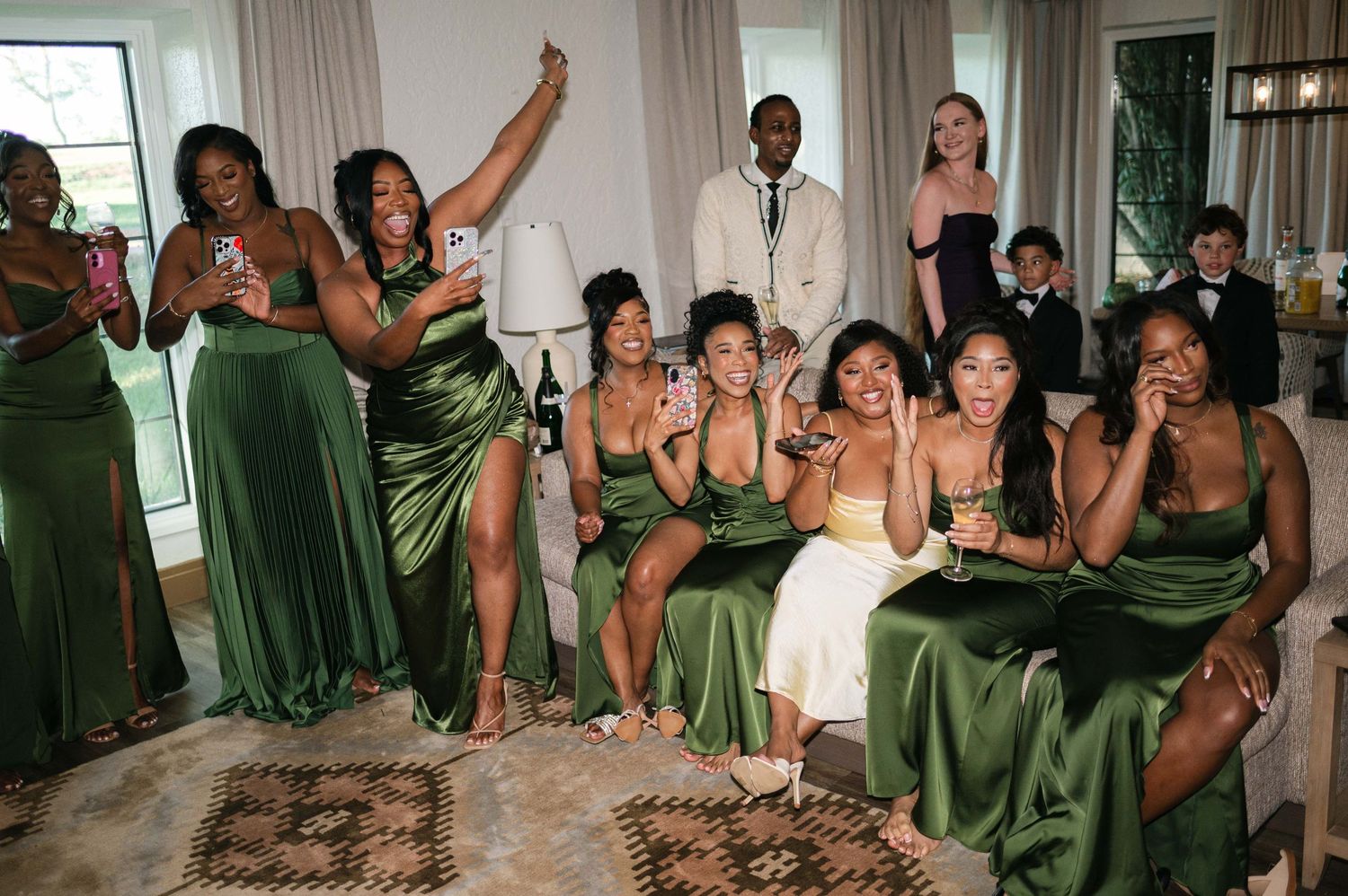 A group of bridesmaids in olive green dresses dance and celebrate at a wedding reception.