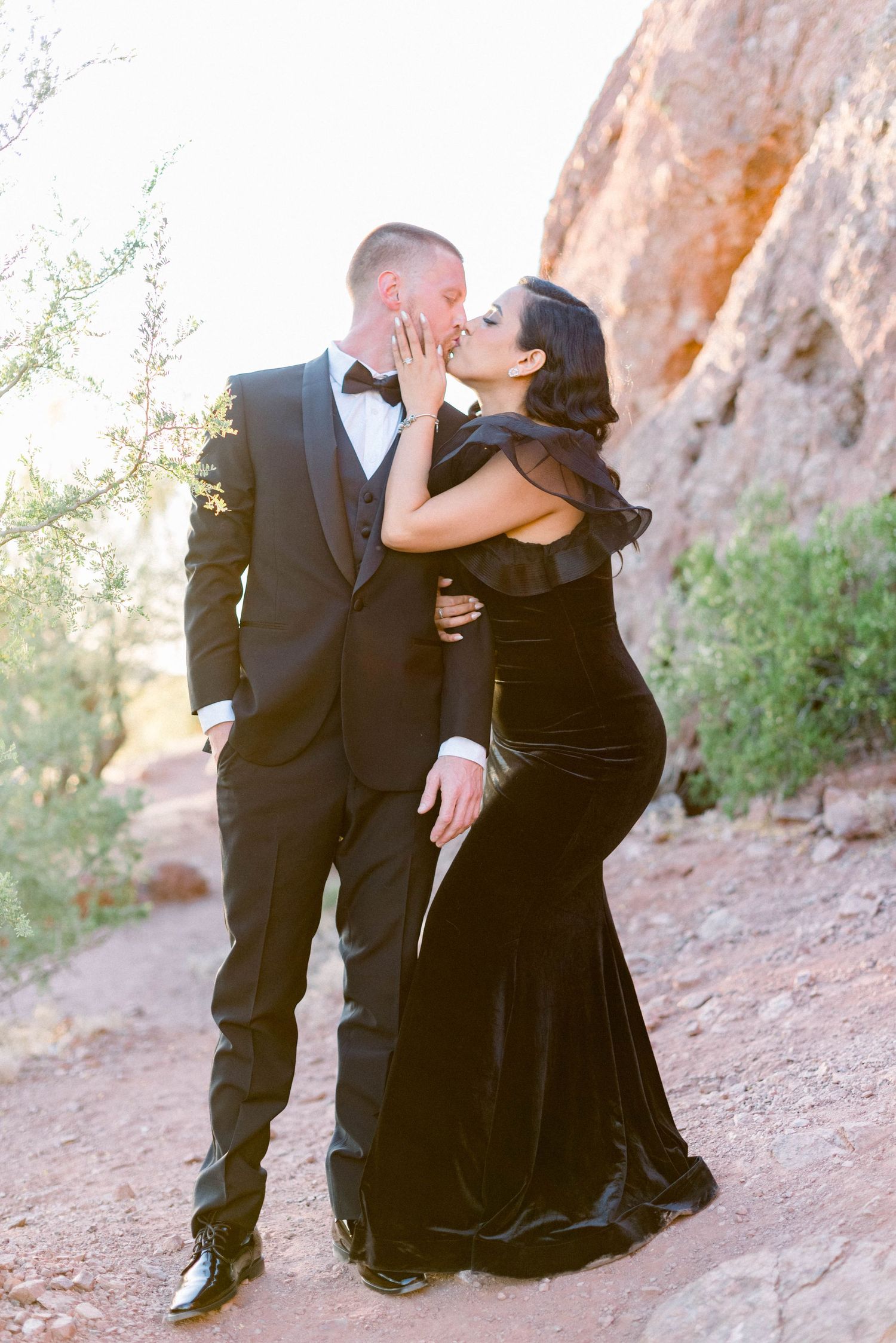 Elegant couple in formal attire embracing against red rock formations.