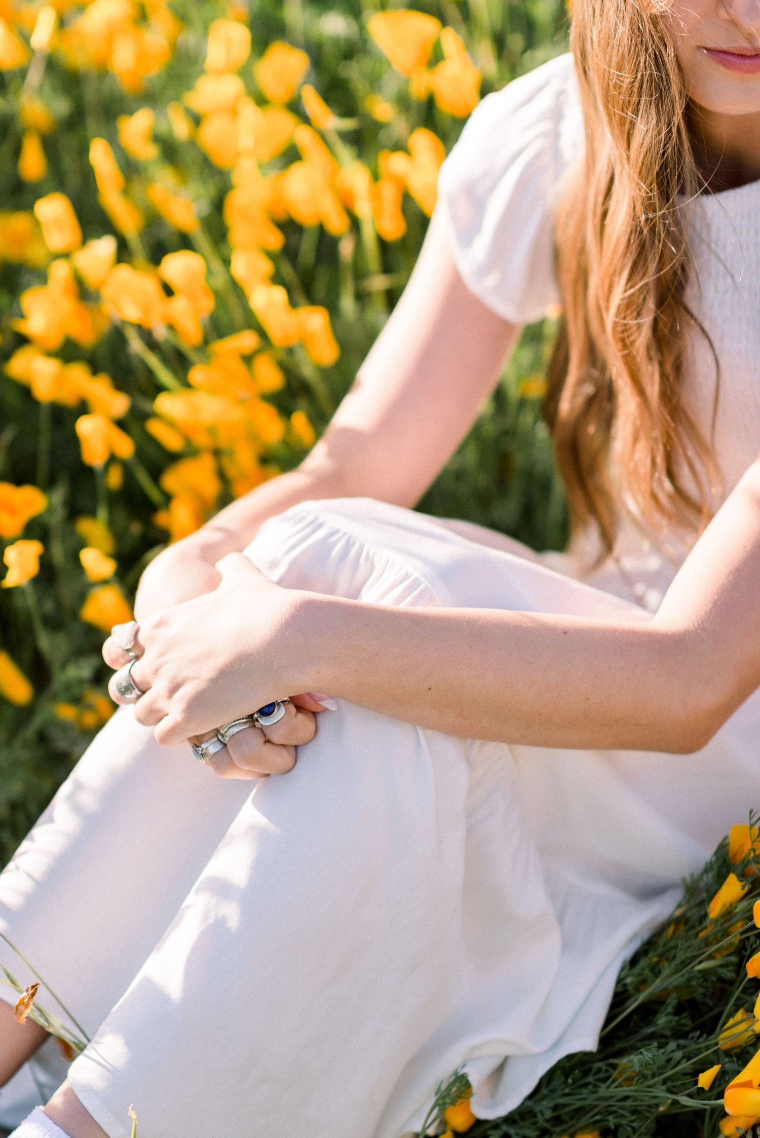 Sitting in a field of yellow wildflowers wearing a white dress with rings on fingers.