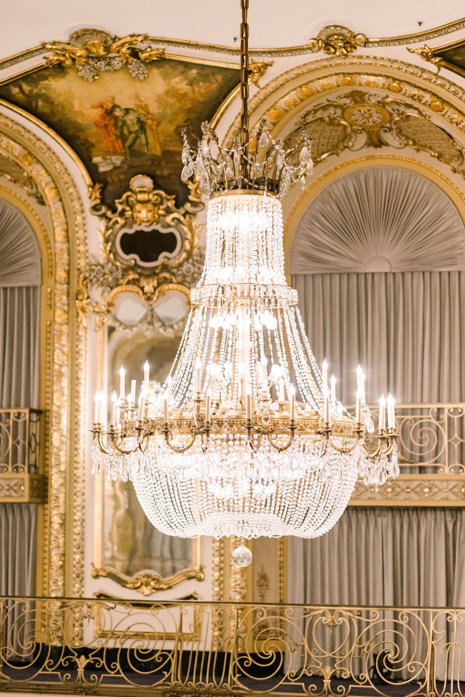 Stunning crystal empire chandelier hanging in an ornate room with gilded architectural details.