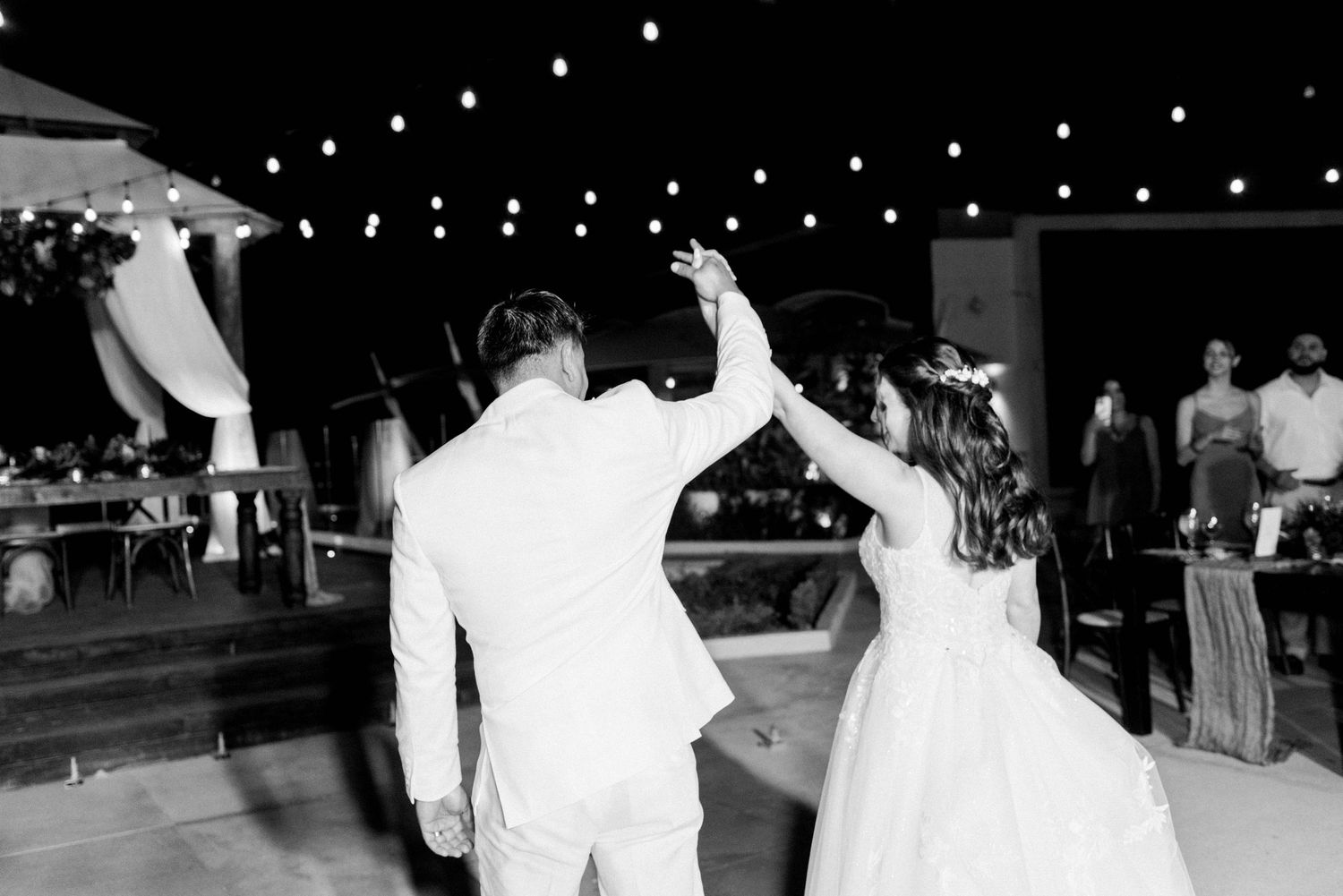Wedding couple dancing under string lights at outdoor reception.