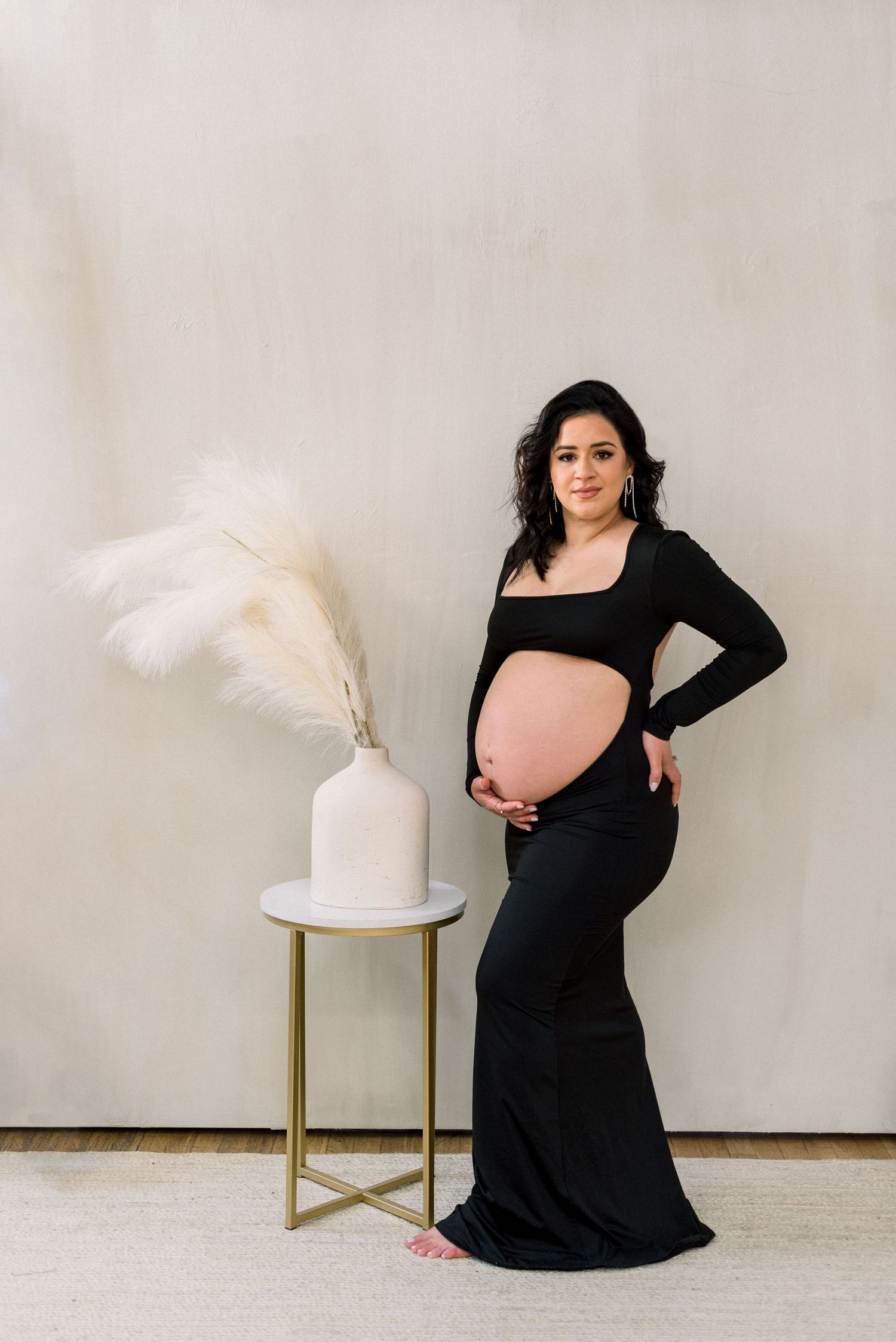 Maternity photo with a long black dress next to a modern side table with pampas grass decor.