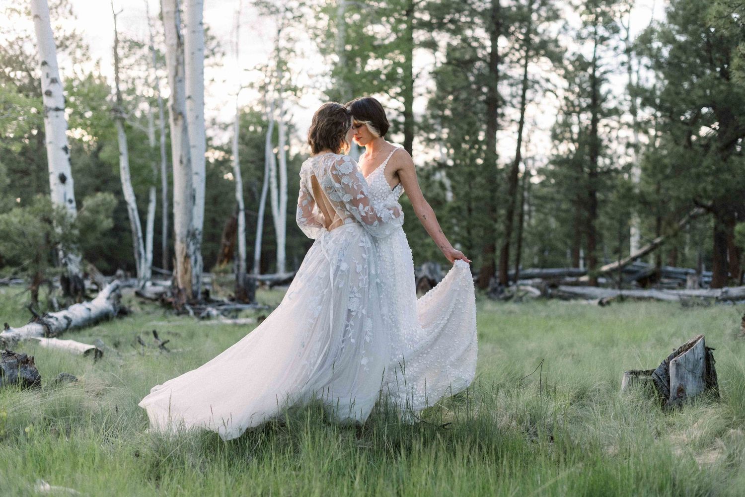 Romantic couple in flowing white dresses dancing together in a forest clearing.