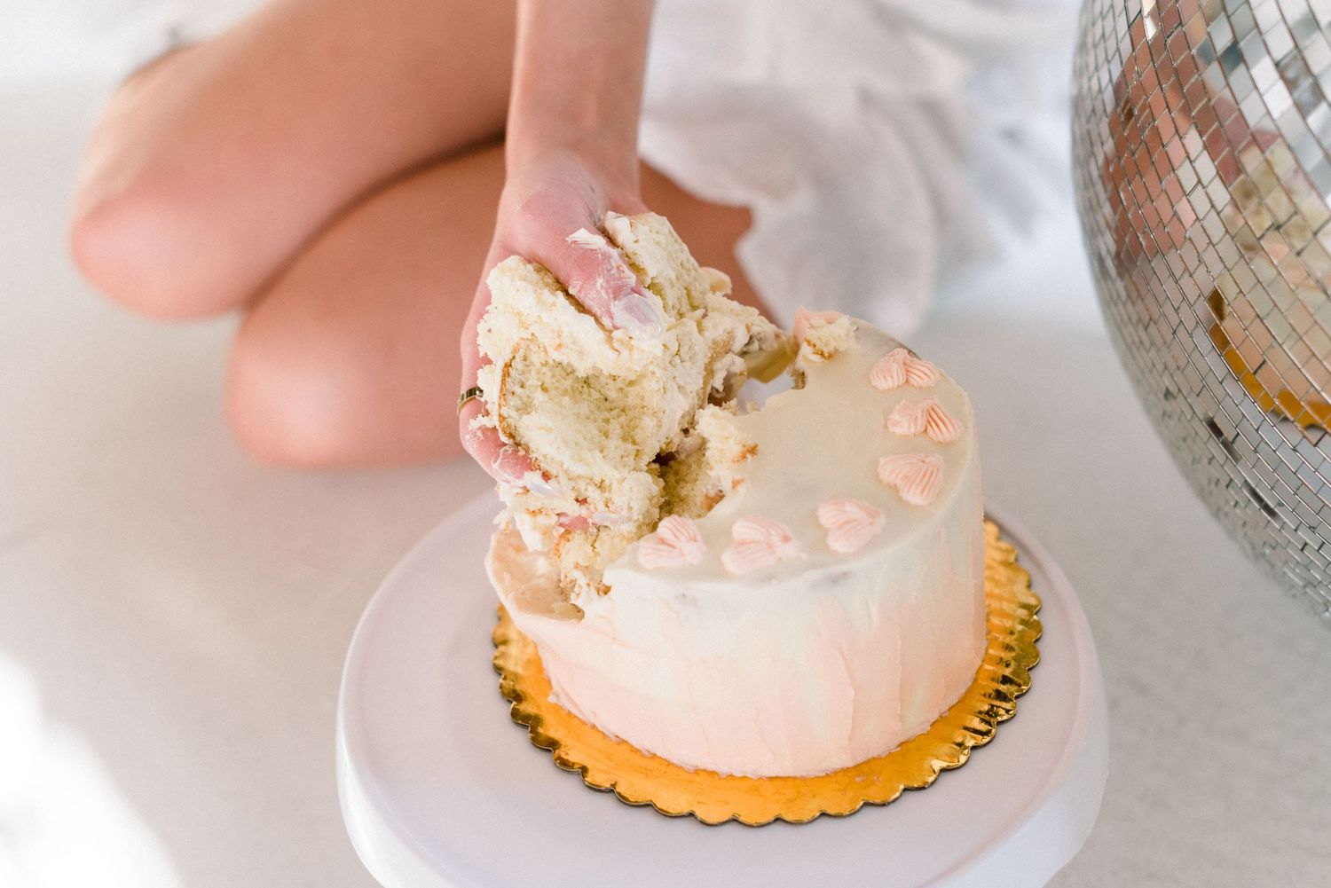 Hand breaking into moist vanilla cake showing layers on white cake stand.