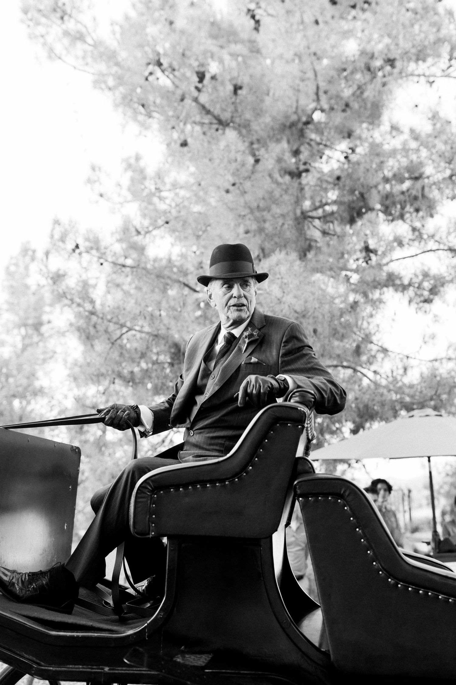 Vintage black and white photo of a gentleman sitting in a carriage wearing a hat and suit.