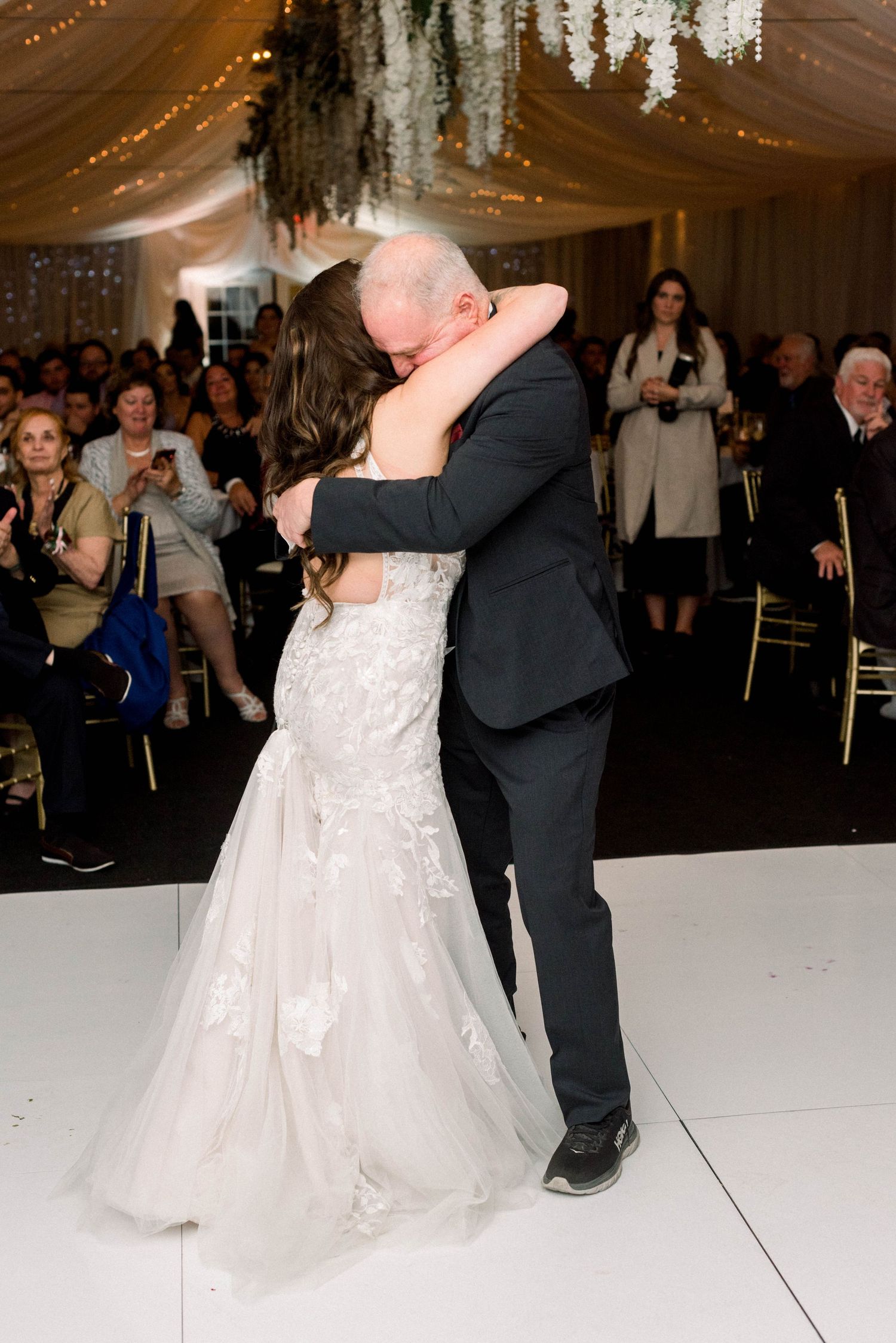 Couple embraces during emotional dance moment at wedding reception under elegant draping and lights.