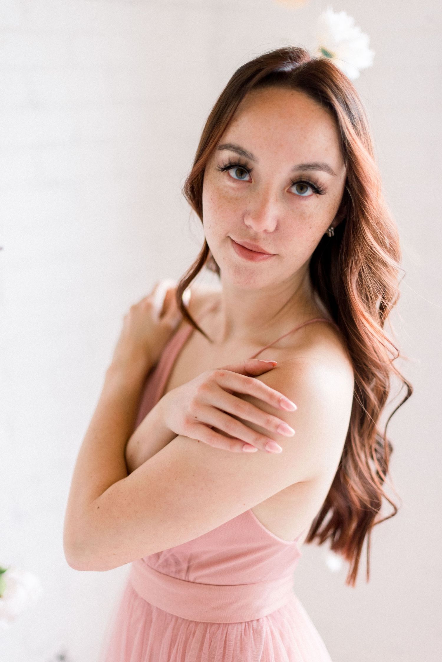 Romantic portrait in pink dress with soft lighting against white background.