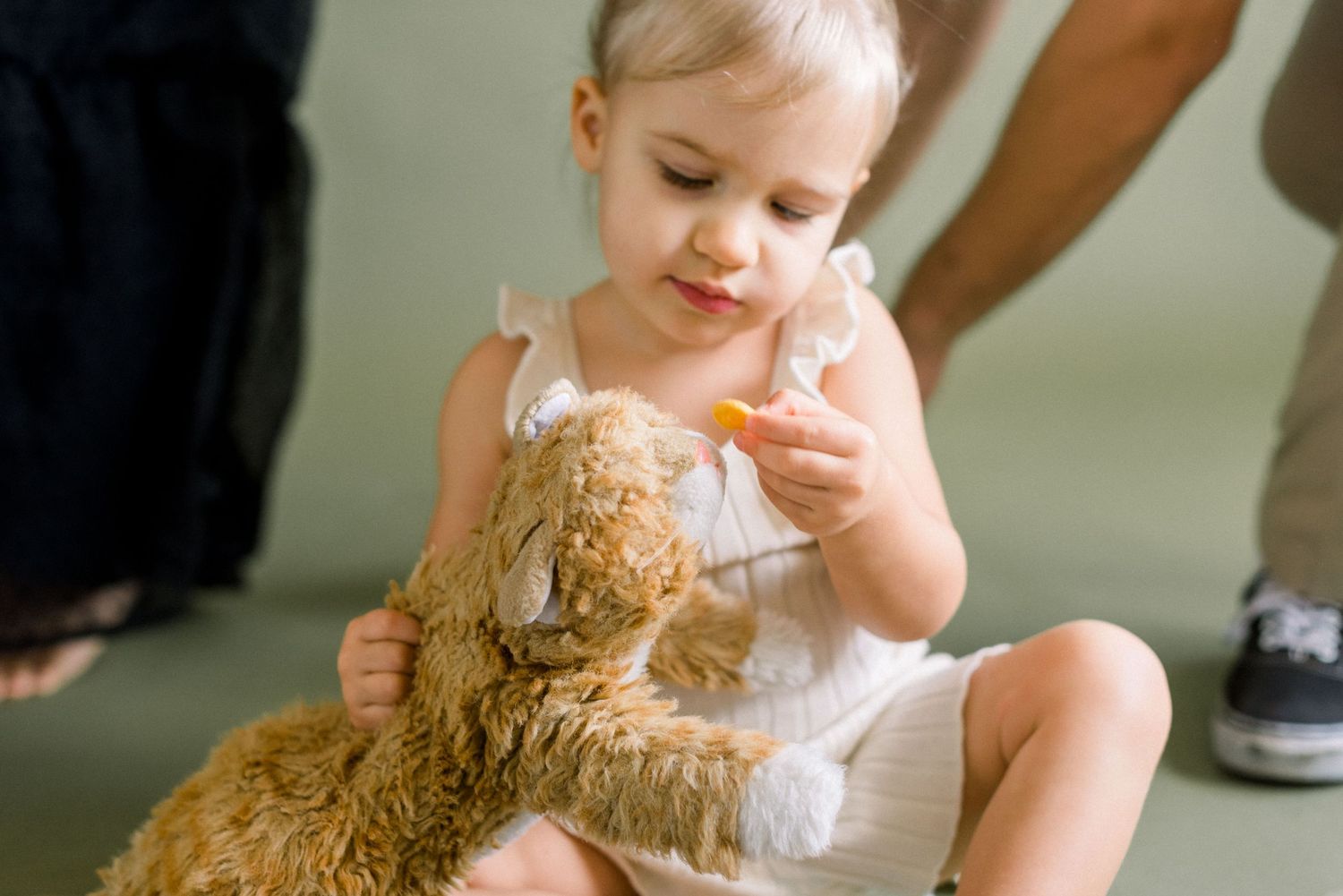 Young child in white dress playing with a stuffed teddy bear during a family photo session.