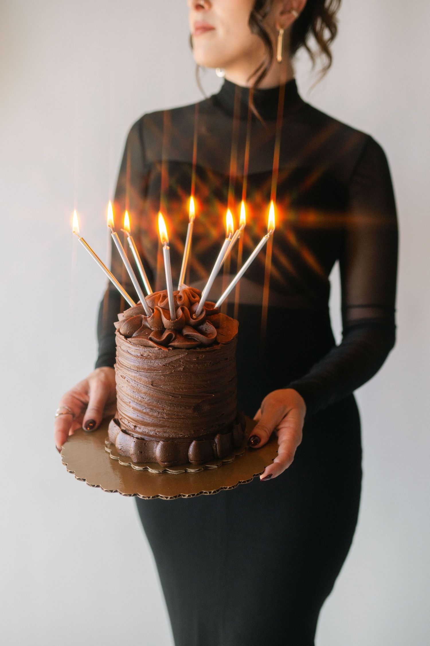 Chocolate birthday cake with lit candles held against white background.