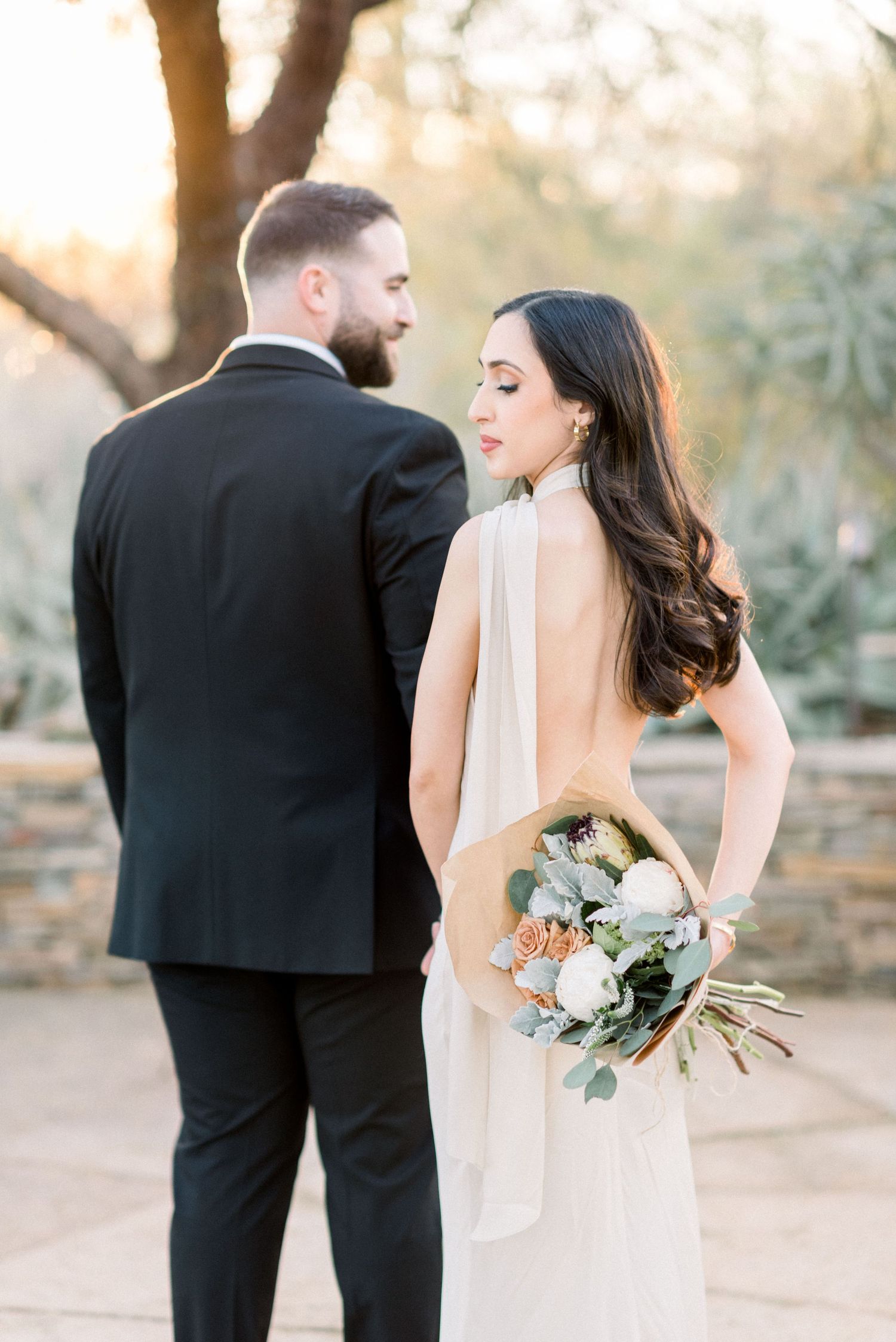 A bride and groom share a romantic moment in a garden setting during golden hour.