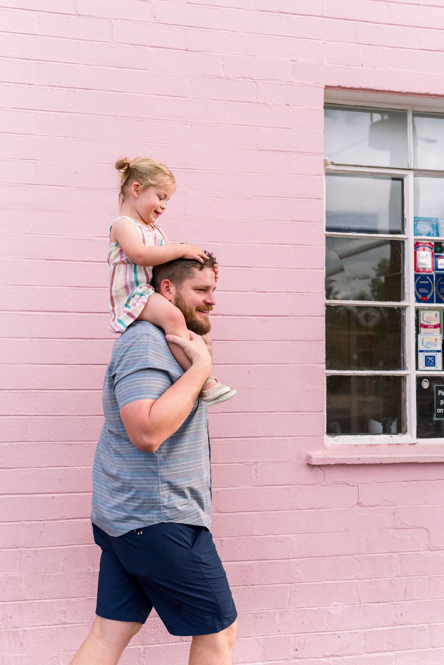 A playful sequence shows a parent carrying a child on shoulders against a pink brick wall.
