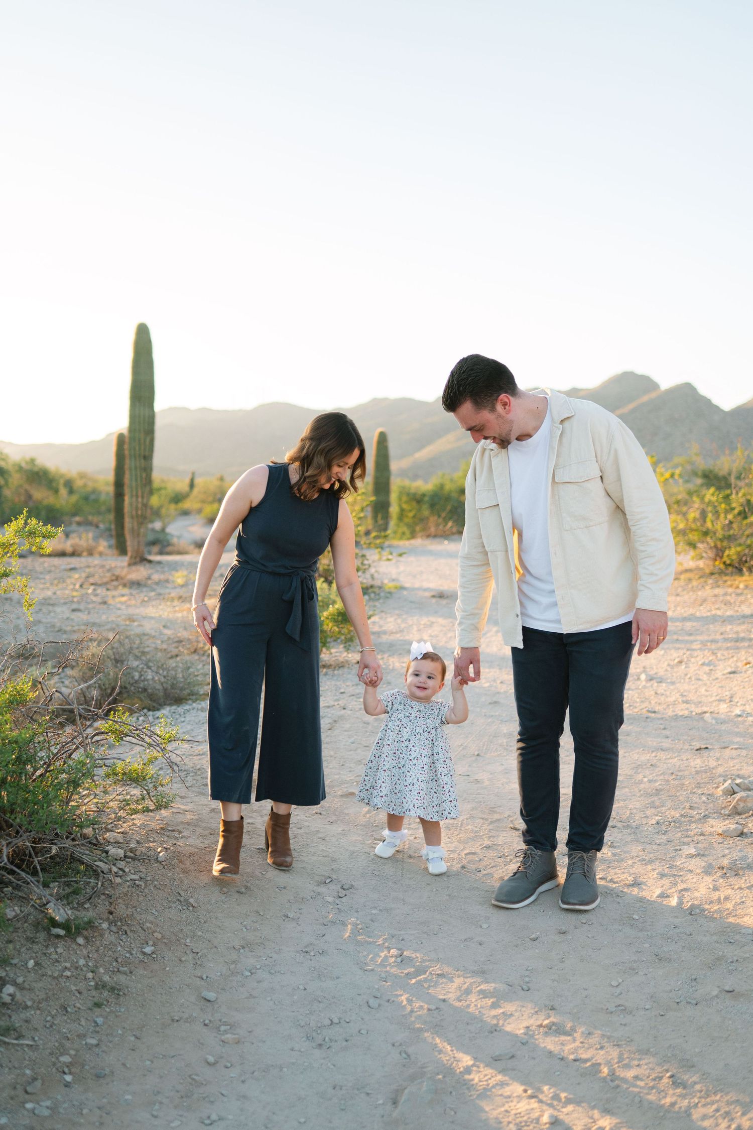 Family walking together on desert trail with saguaro cactus and mountains in golden evening light.