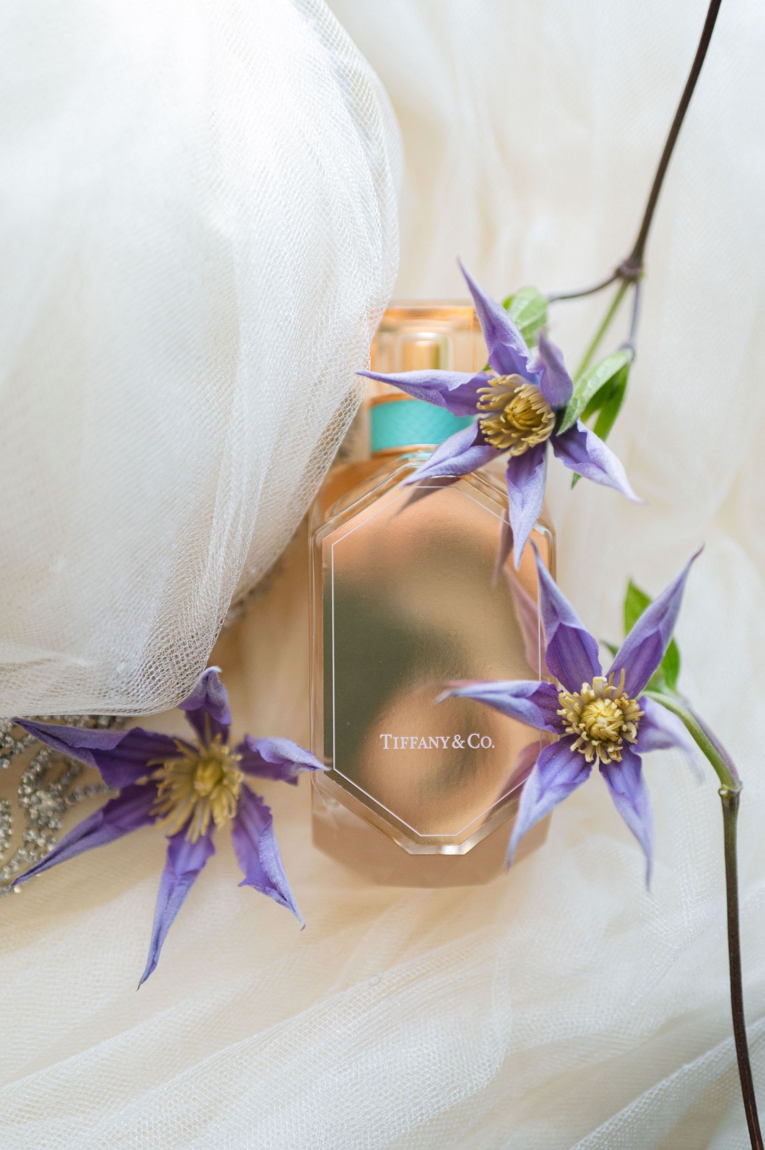 Tiffany & Co perfume bottle with purple clematis flowers arranged on white tulle fabric.