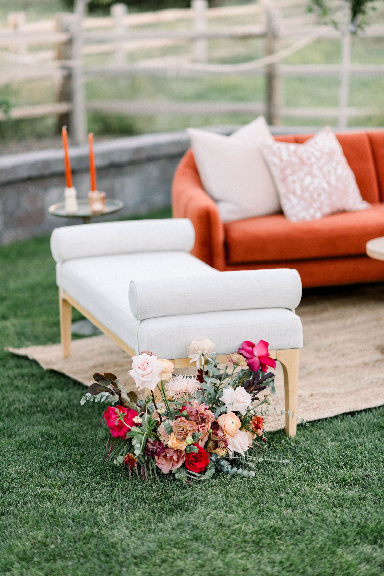 Modern lounge seating area with white and coral cushions decorated with floral arrangements on grass.