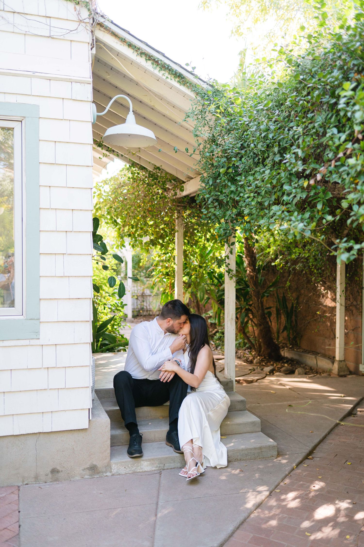 Couple shares a tender moment in a garden setting with white architectural details.