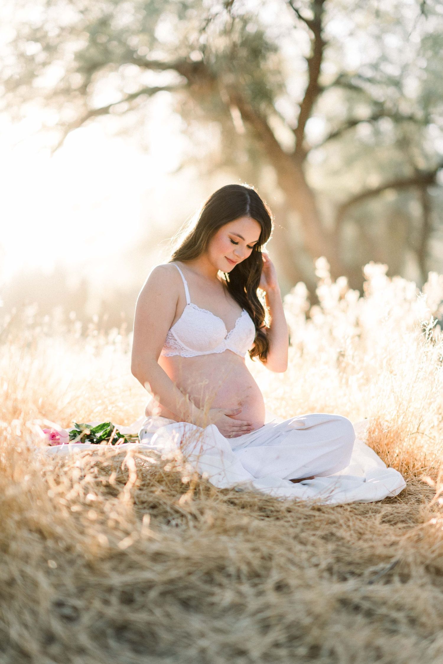 Ethereal maternity photo in a sunlit field featuring flowing white dress and golden light.