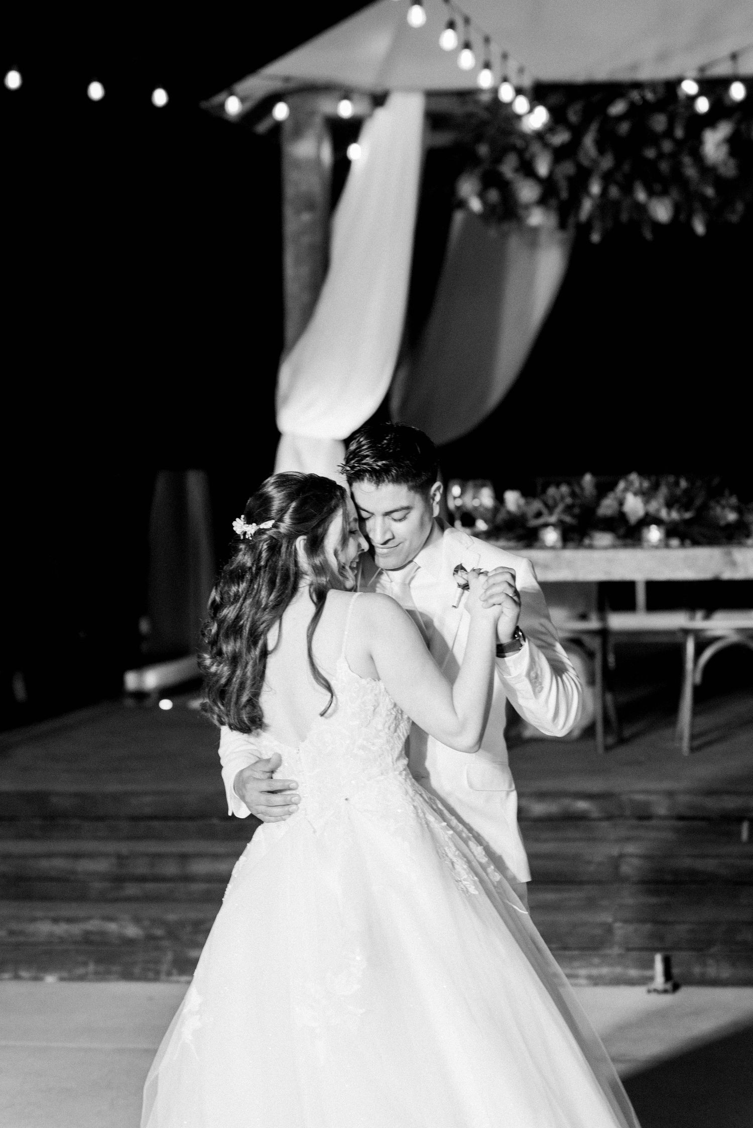 Black and white photo of couple sharing first dance under outdoor pavilion.