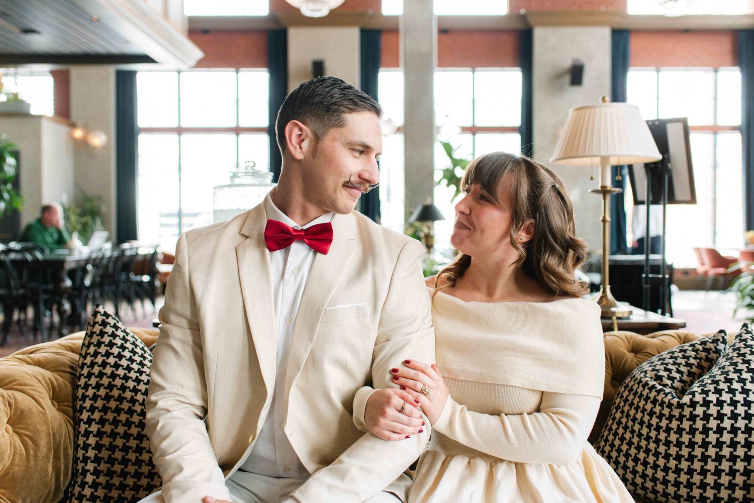 A couple in matching white formal wear shares a loving moment on a houndstooth patterned couch.