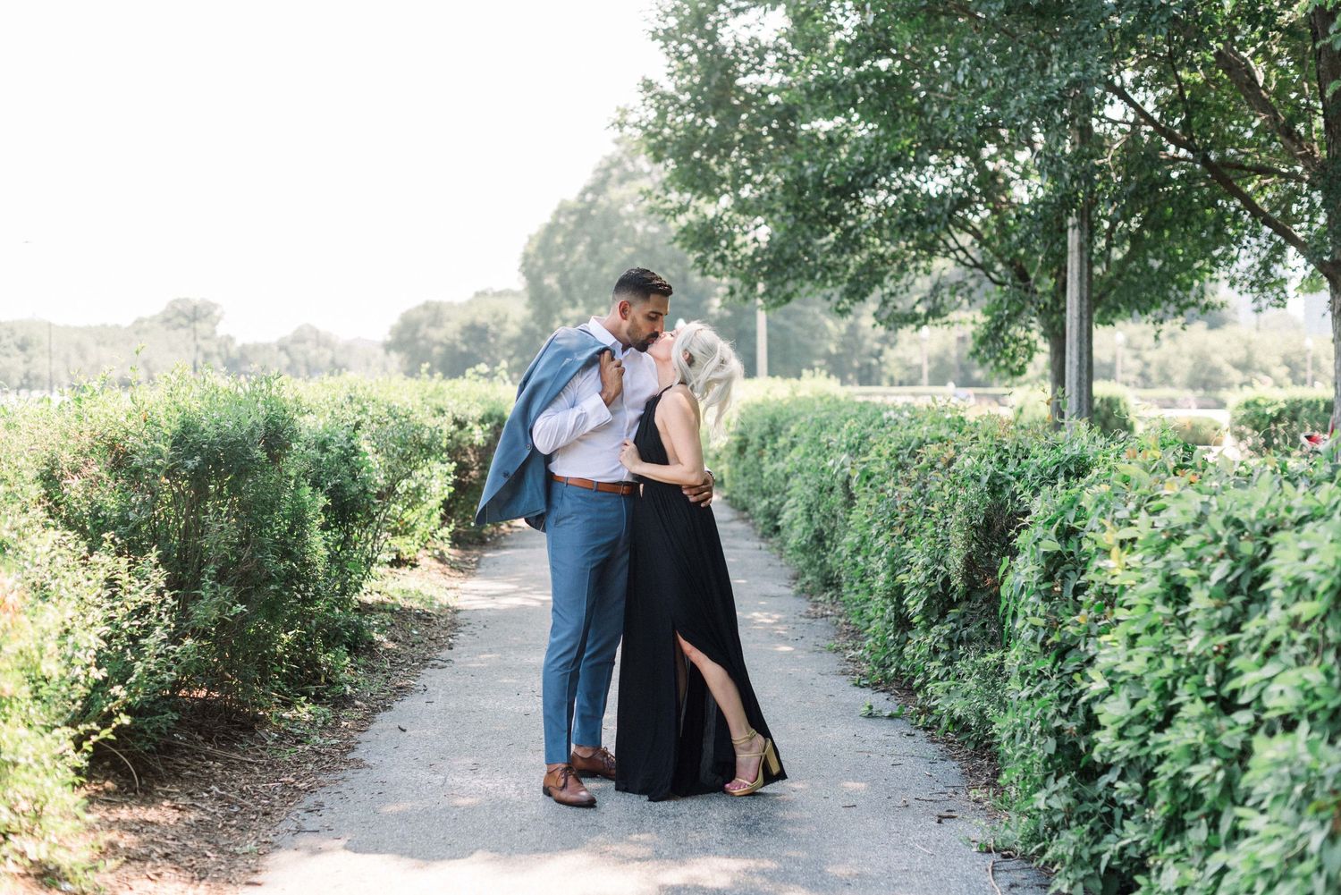 Couple embracing on garden path surrounded by green hedges and trees.