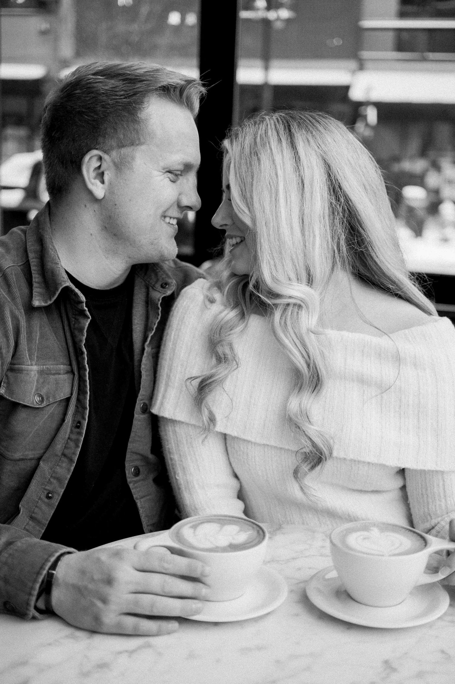 A couple shares laughter over coffee at a cafe with marble tables.