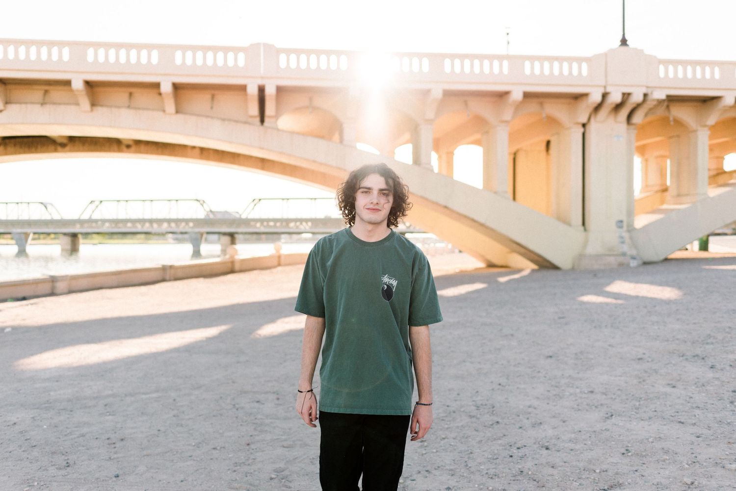 Person in green t-shirt standing under concrete overpass bridge in soft lighting.