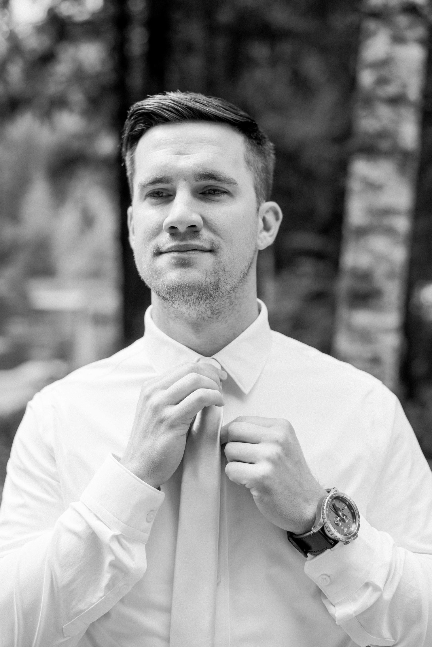 Groom adjusting his light pink tie while wearing a crisp white dress shirt.