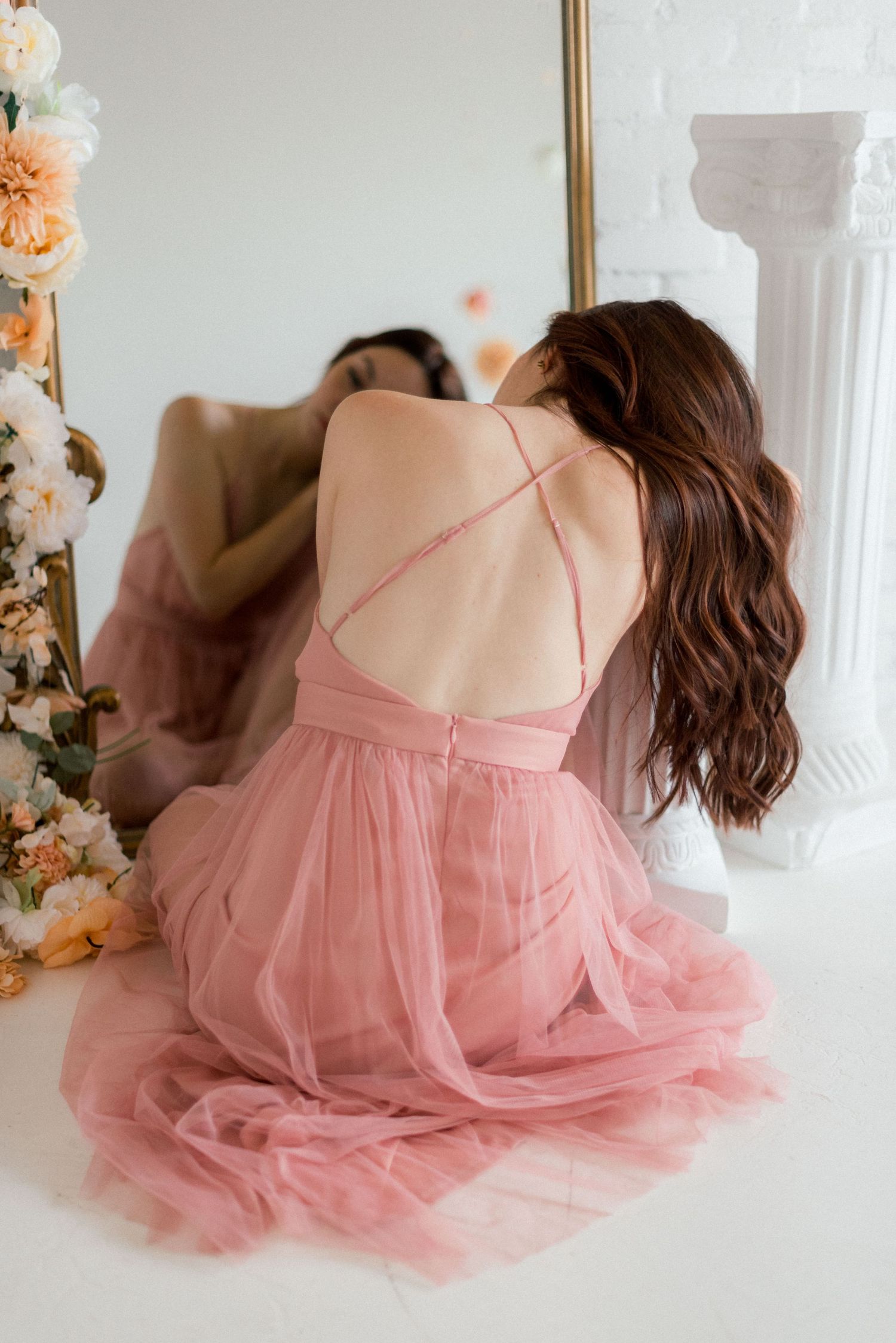 Back view of flowing pink tulle dress with delicate strappy details in front of mirror.